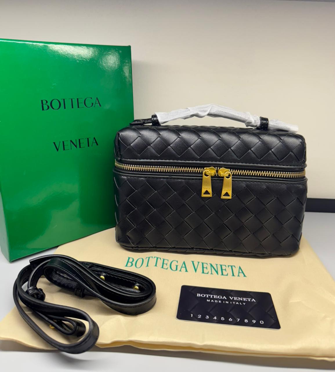 Black woven handbag with gold zipper, green box, and beige pouch on a white background