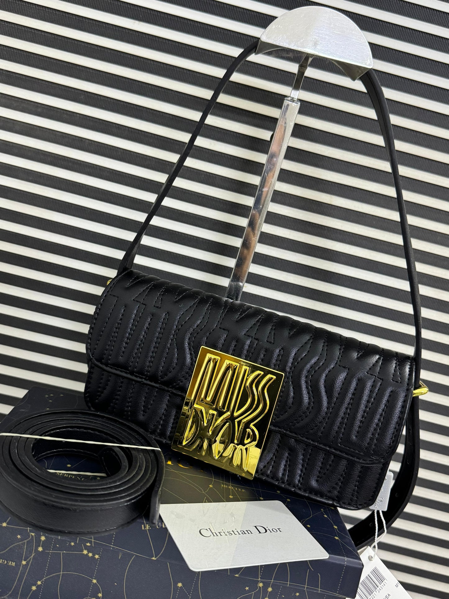 Black handbag with gold logo on a striped background