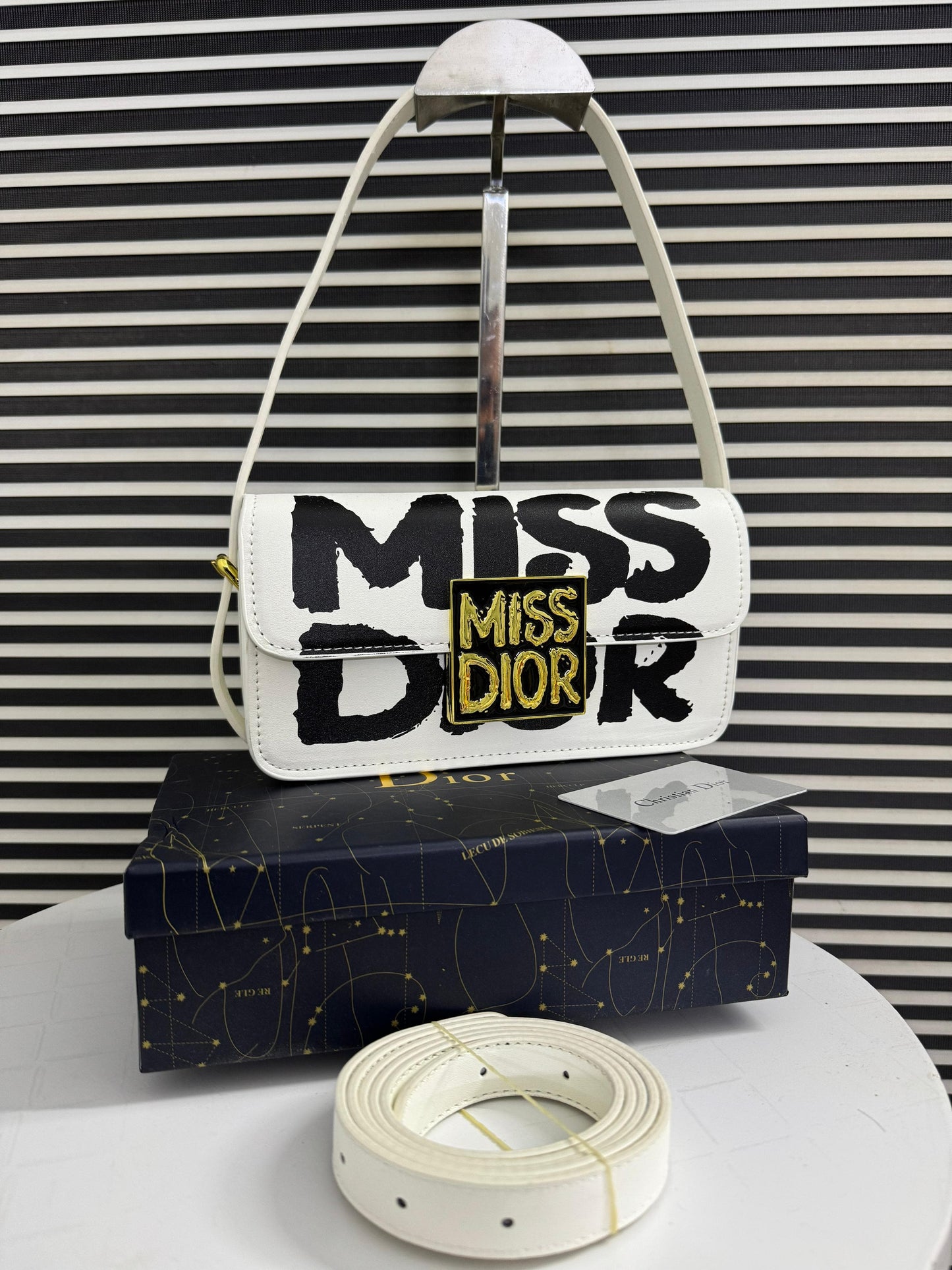 White handbag with 'MI SS DI OR' text on a black and white striped background