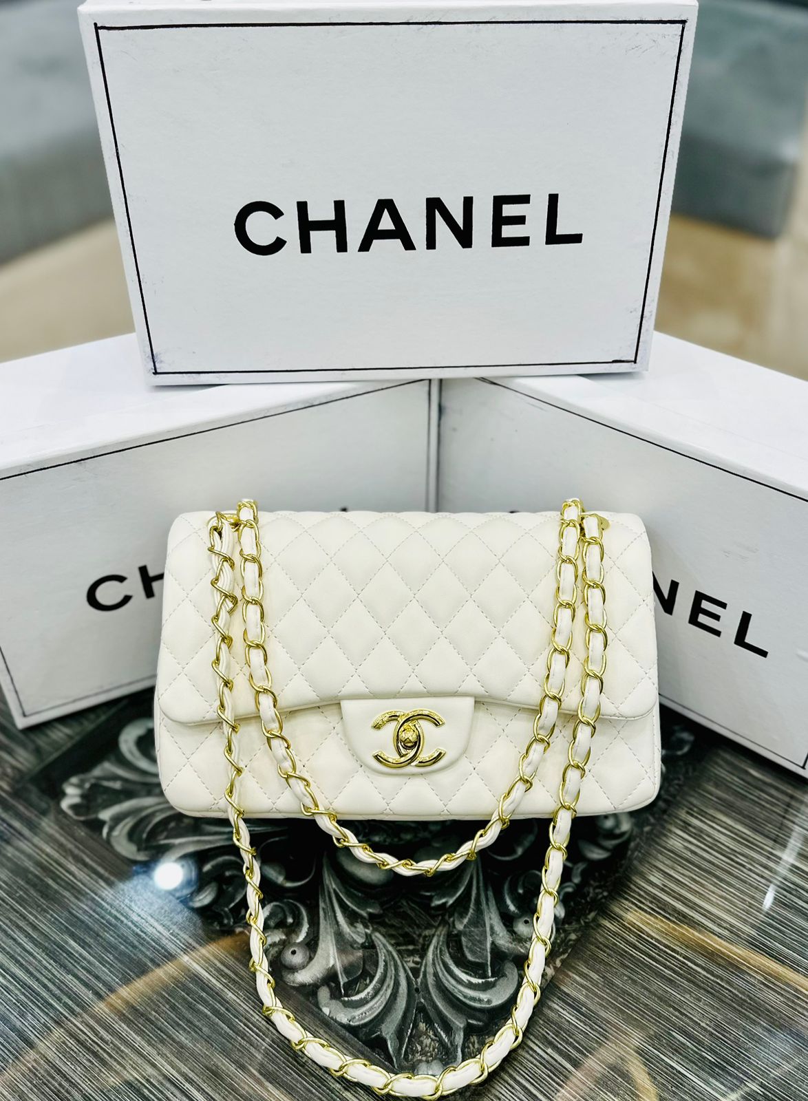 White Cha nel handbag with gold chain on a reflective surface with Cha nel branding in the background.