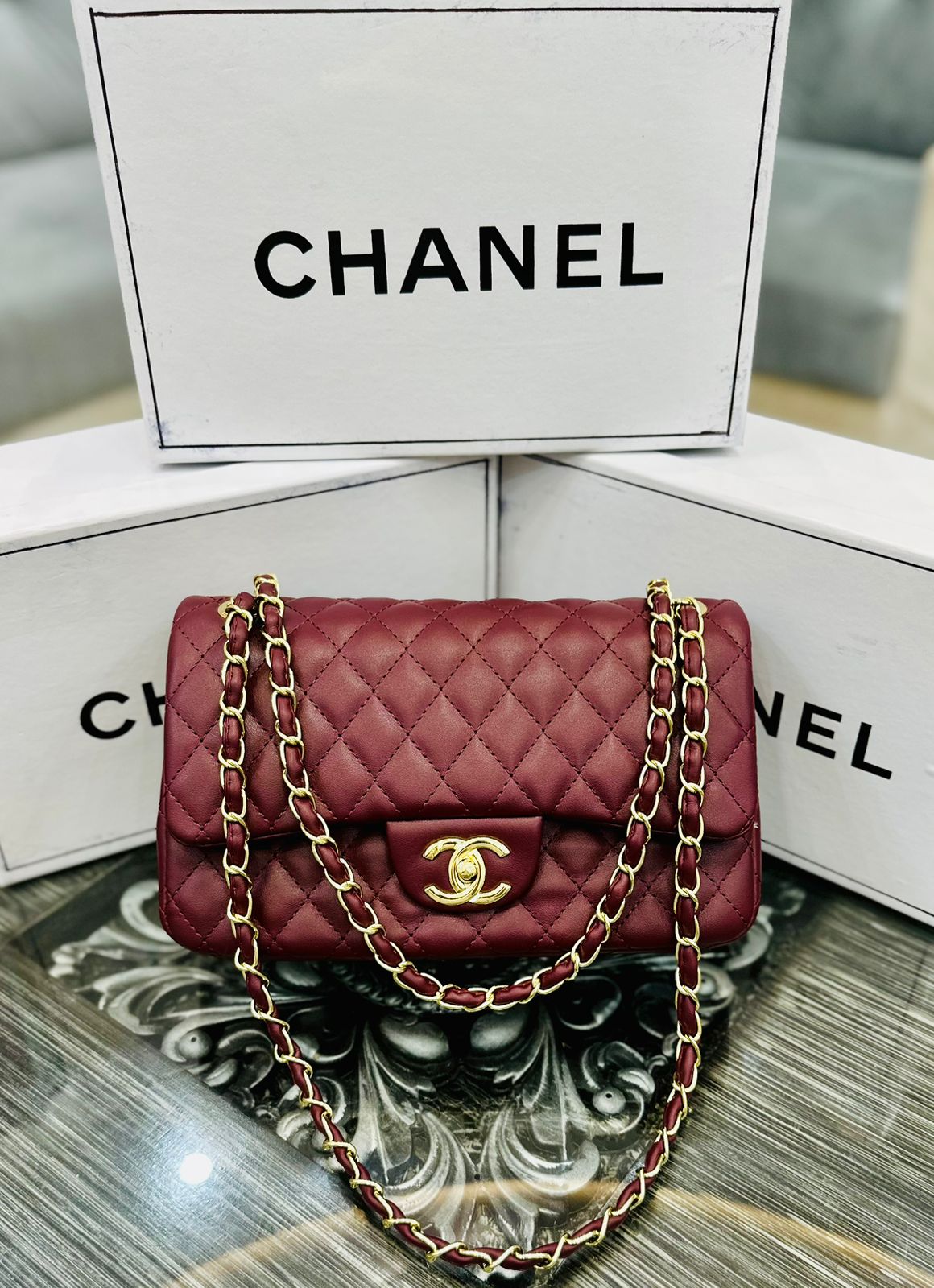 Red quilted handbag with gold chain and Cha nel logo on a reflective surface with Cha nel branding in the background.