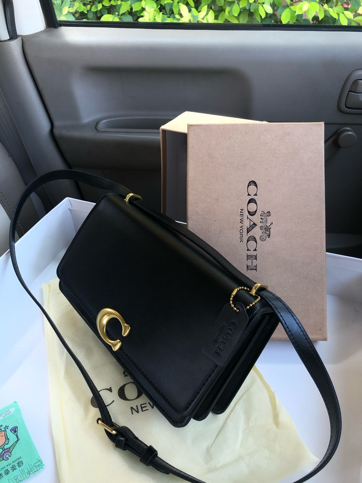 Black handbag with gold accents on a white surface next to a Co ach box.