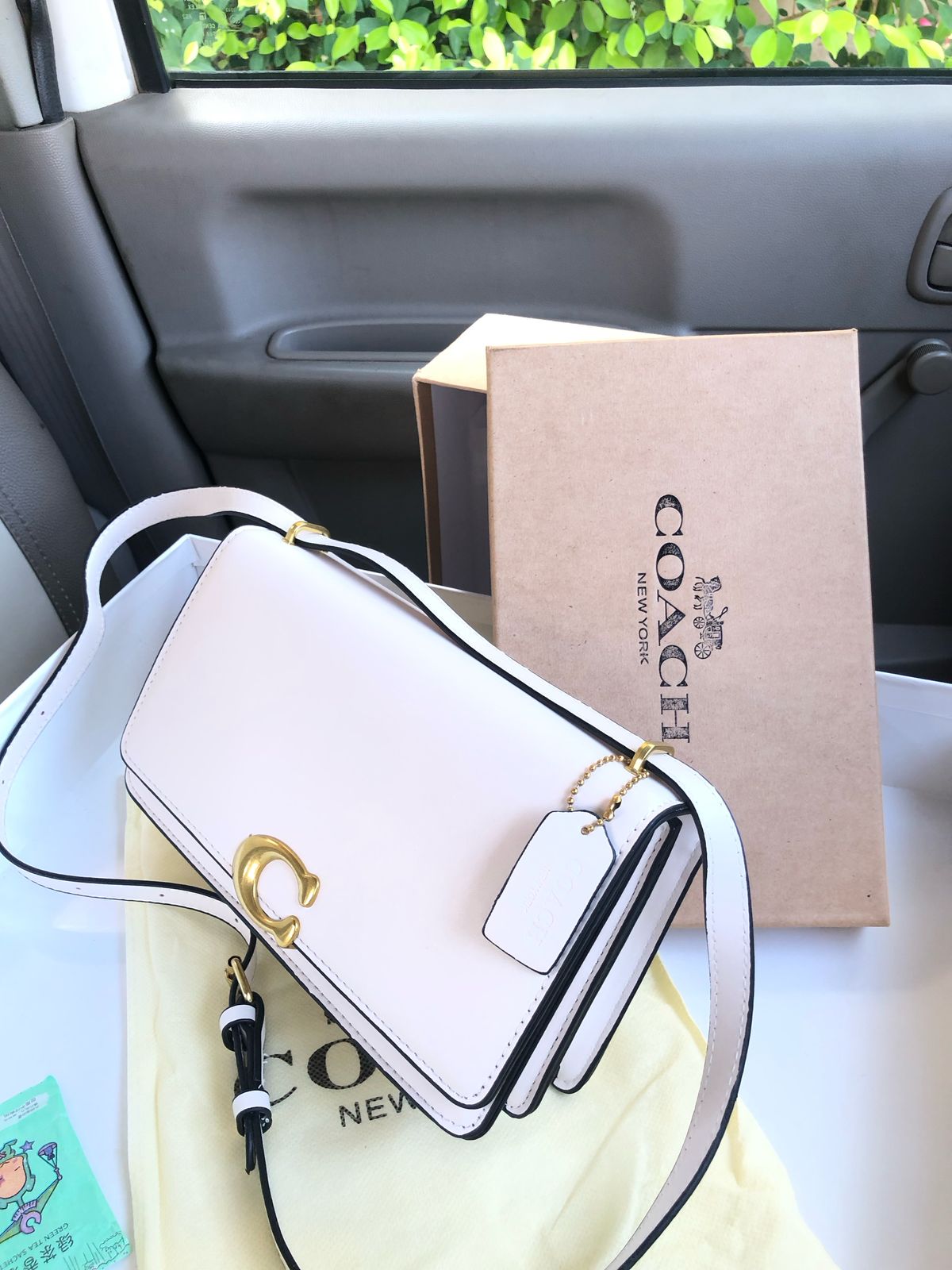 White handbag with gold accents and Co ach box in a car.