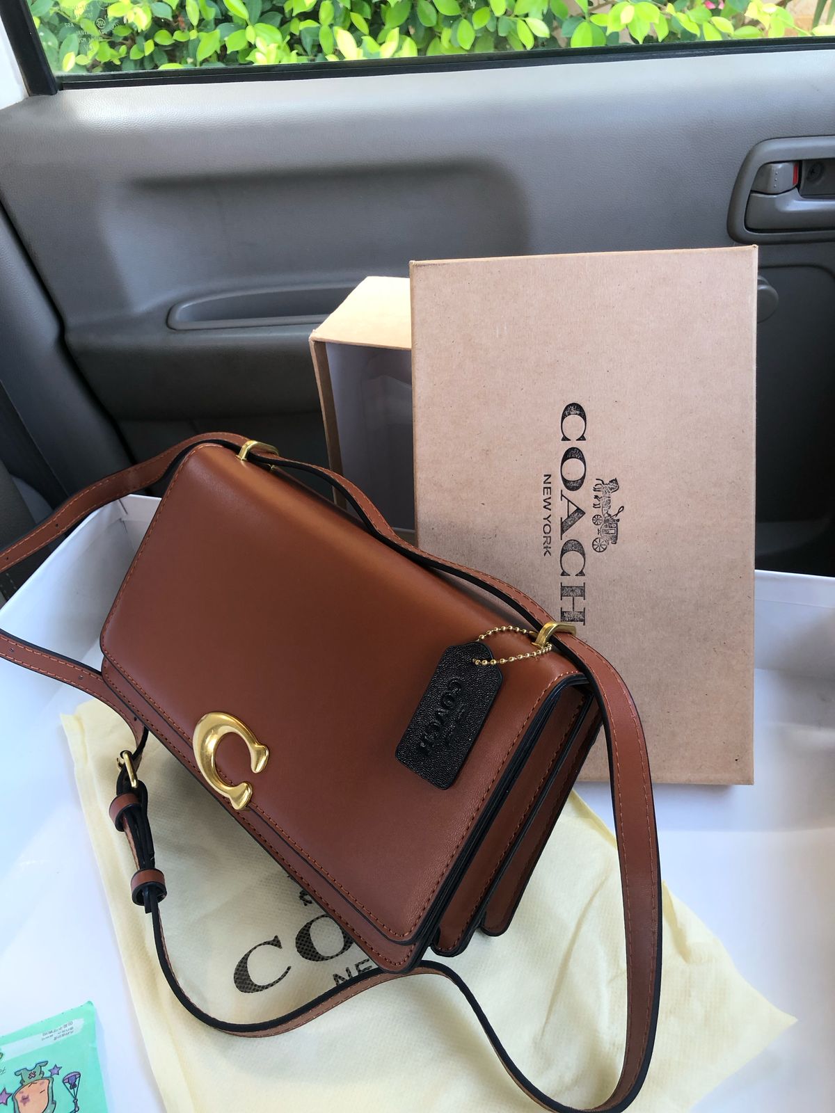 Brown Co ach handbag with a matching box on a car seat.