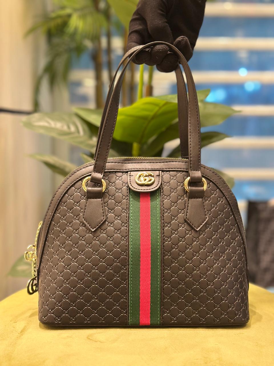 Brown Gucci handbag with a red and green stripe held by a gloved hand.