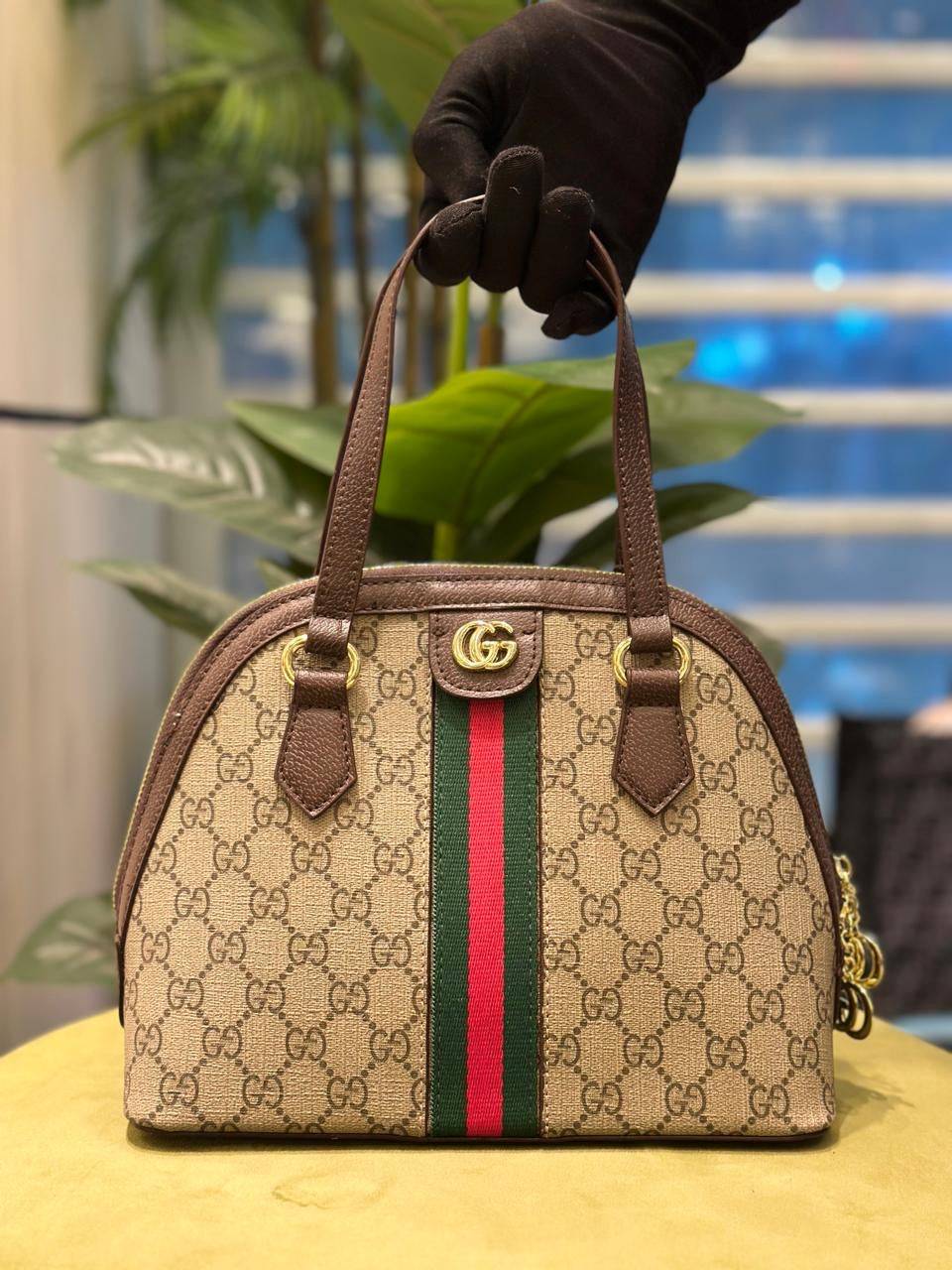 Guc ci handbag with distinctive pattern and color stripe held by a gloved hand.