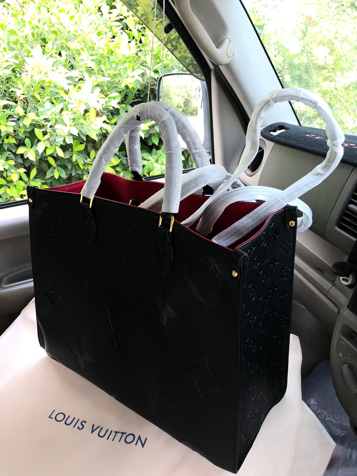 Black Lou is Vui tton handbag with a red interior on a car seat.