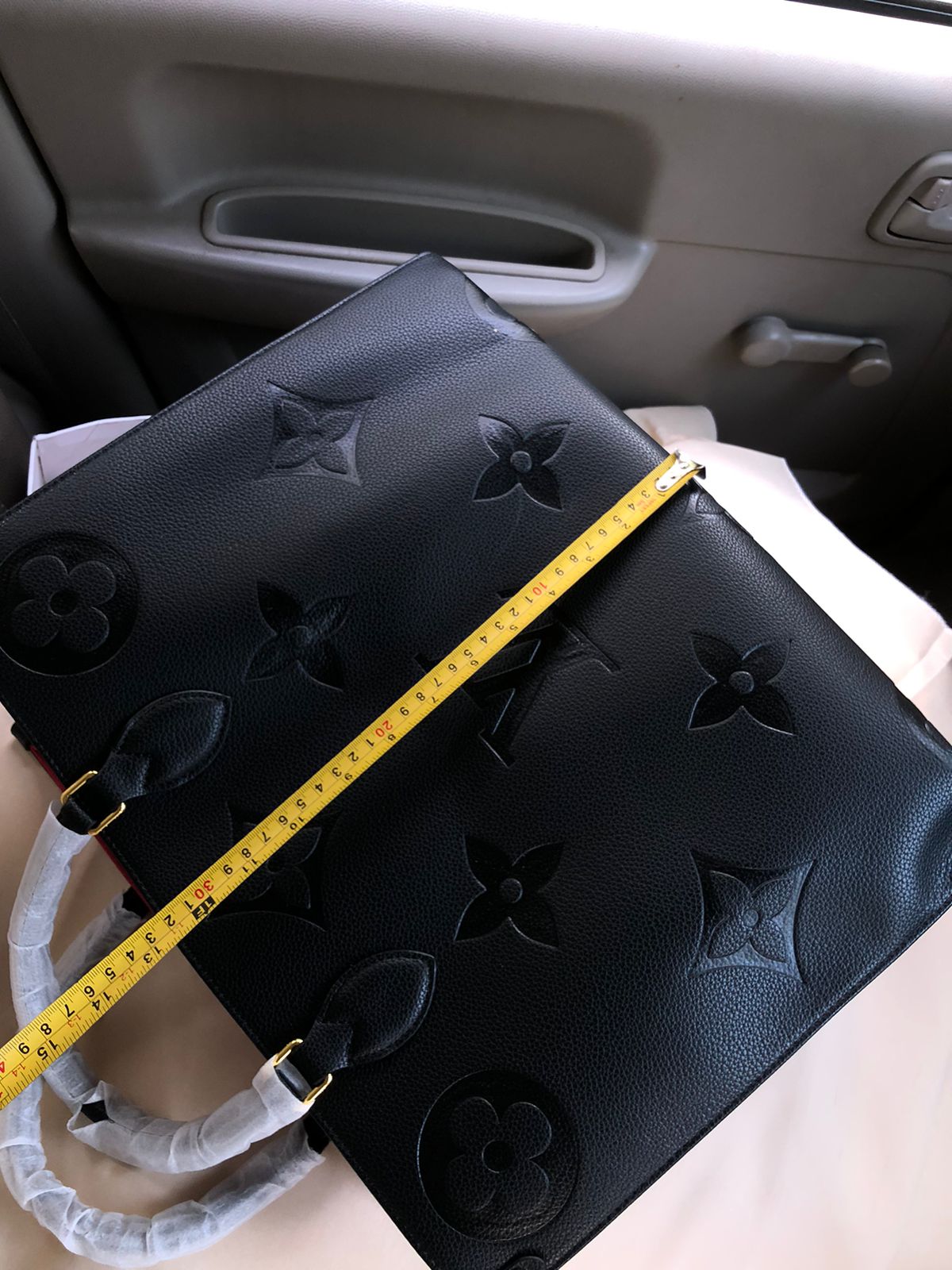 Black leather bag with floral embossing and a measuring tape on a car seat.