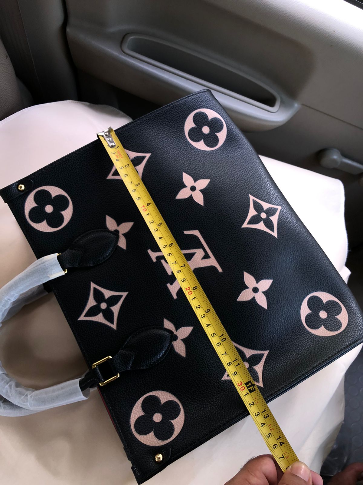 Black handbag with pink floral patterns and a measuring tape on a car seat.