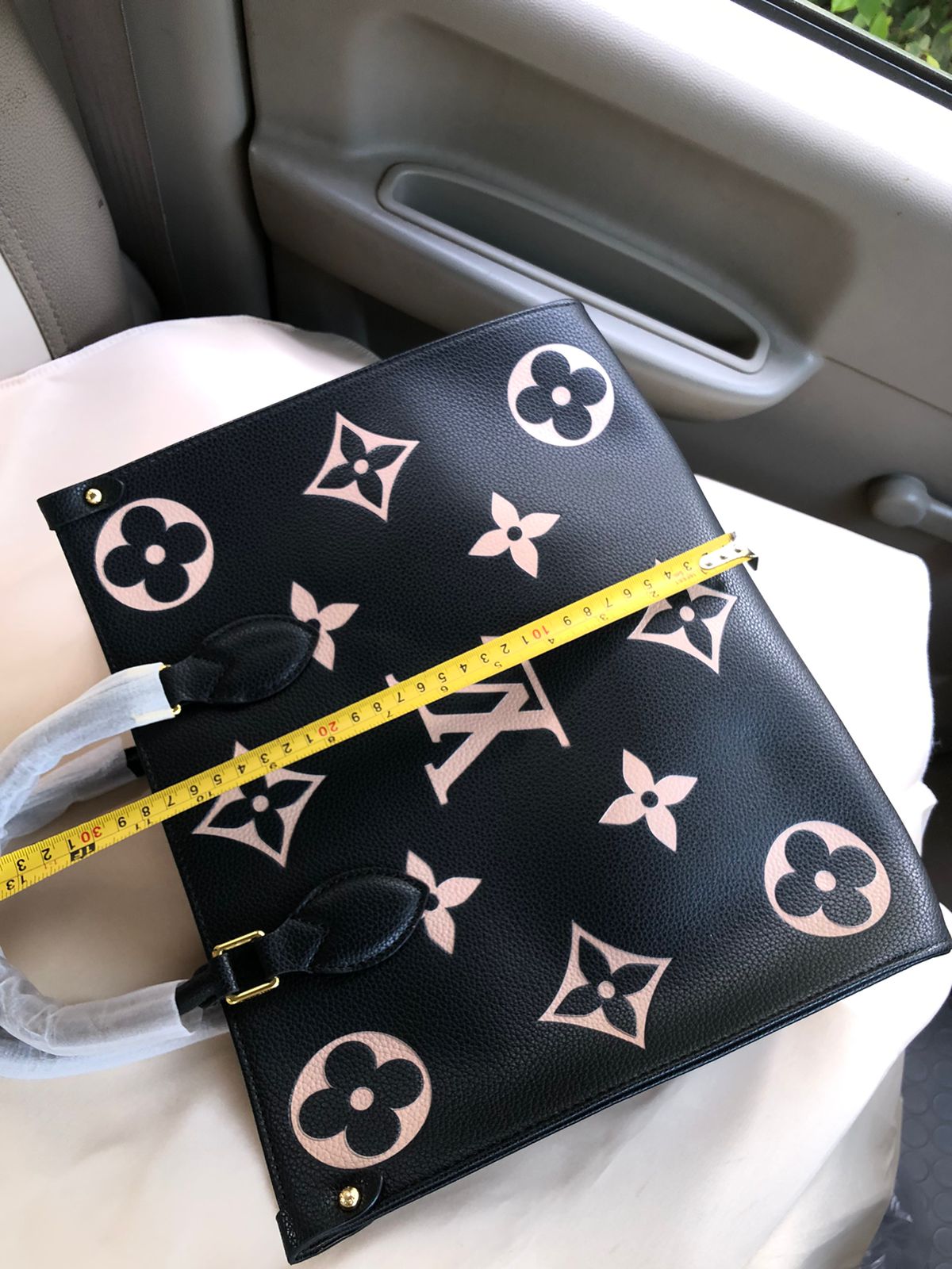 Designer handbag with monogram pattern and measuring tape on a car seat.
