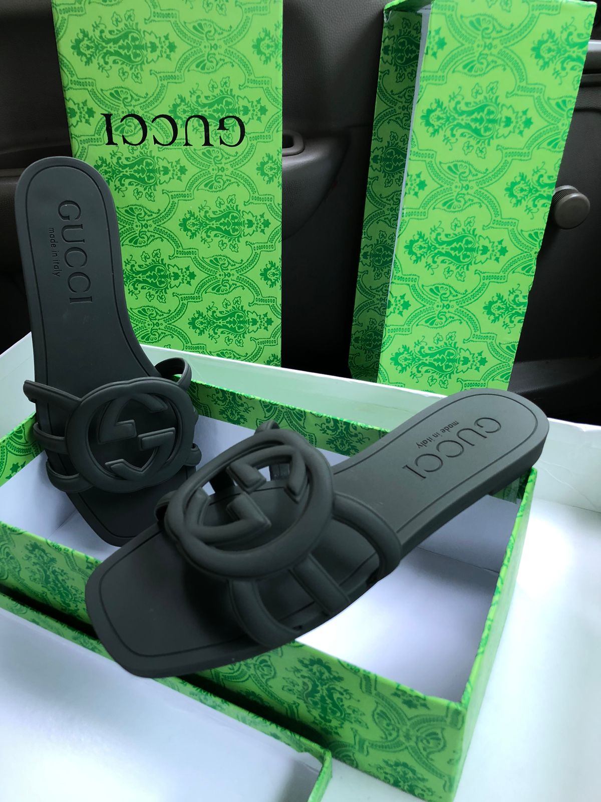 Black sandals with Guc ci logo on a green box with Guc ci branding.