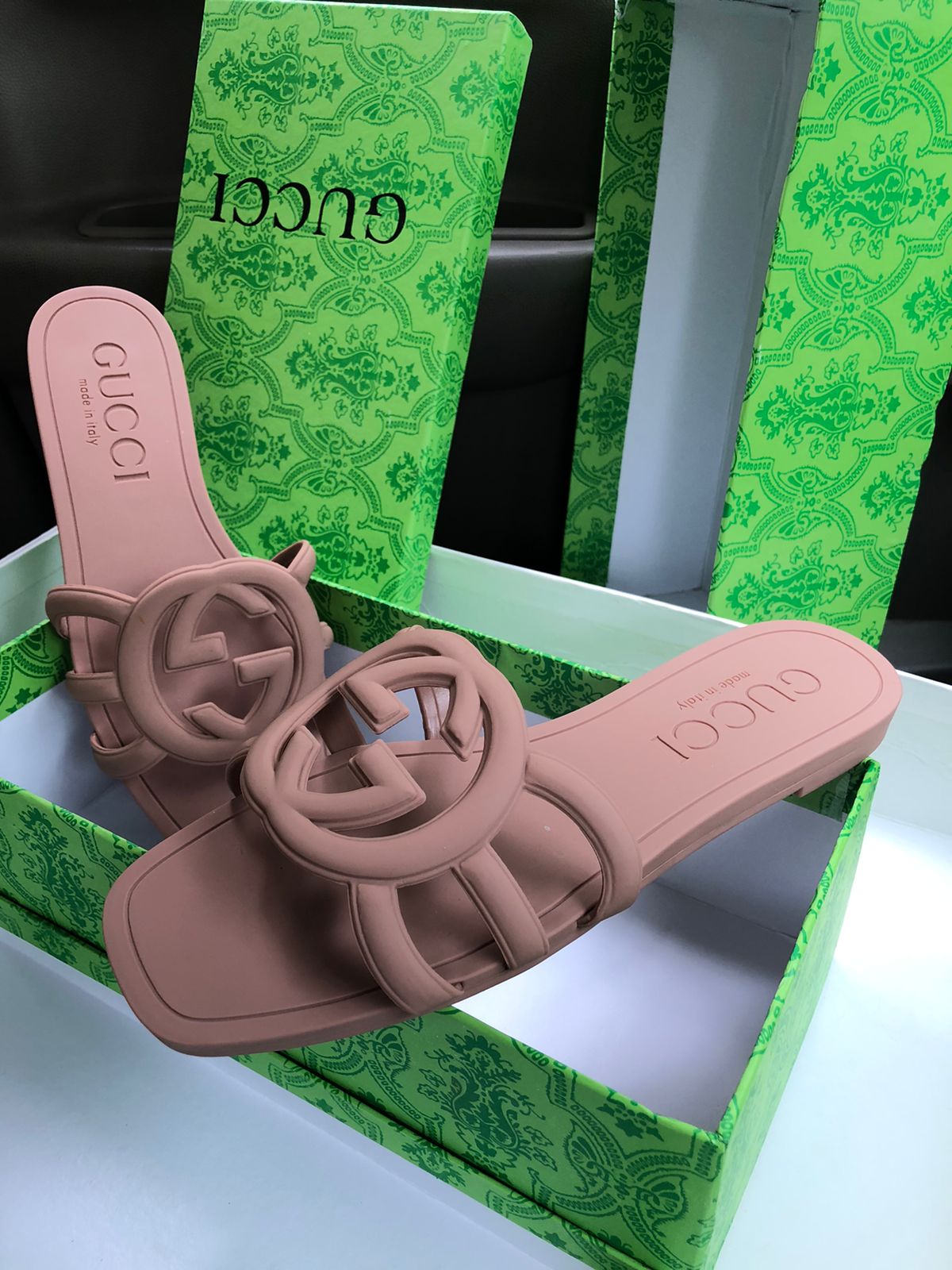 Brown Guc ci sandals on a white surface with green packaging in the background