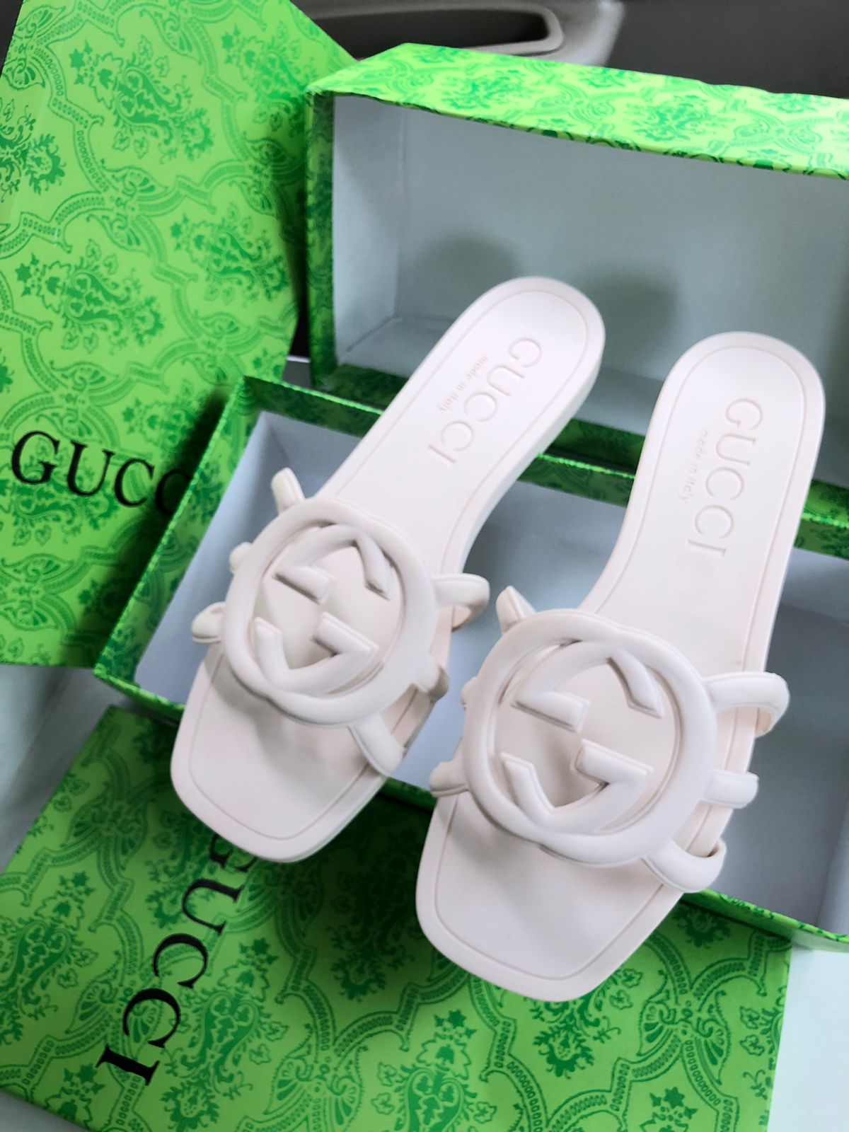 White sandals with decorative rings on a green Guc ci box