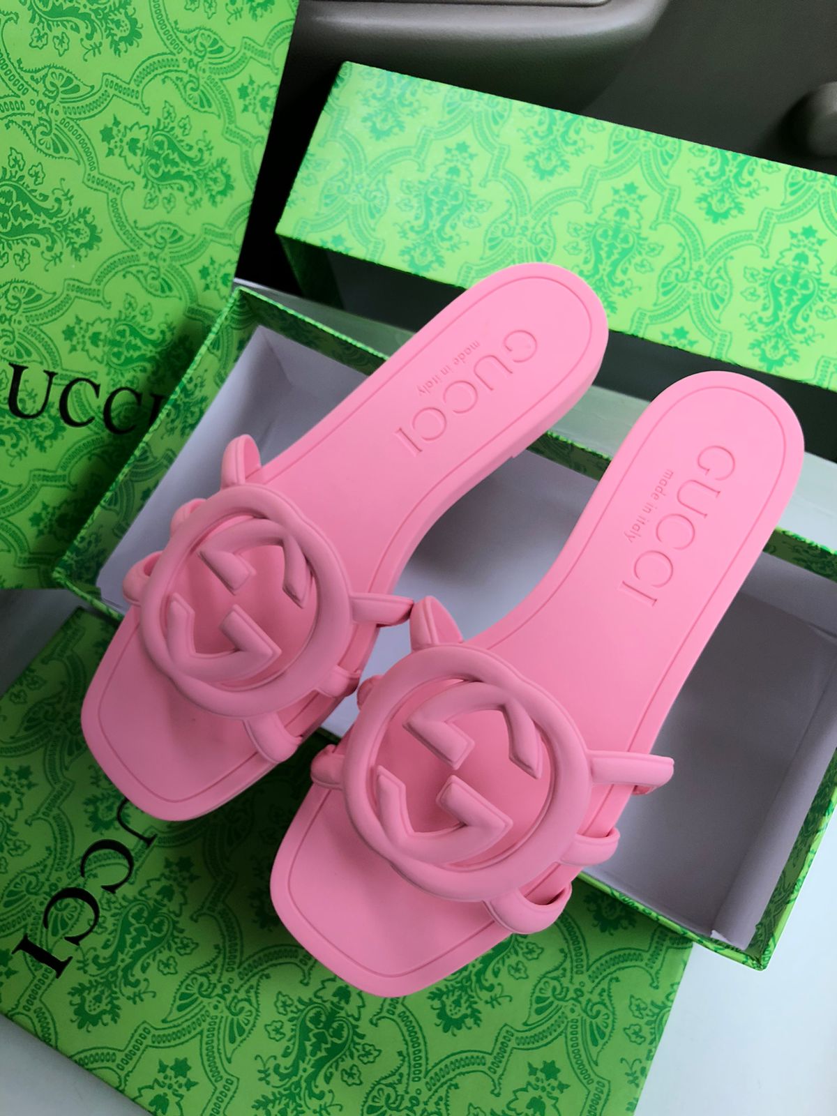 Pink sandals with floral designs on a green box with branding.