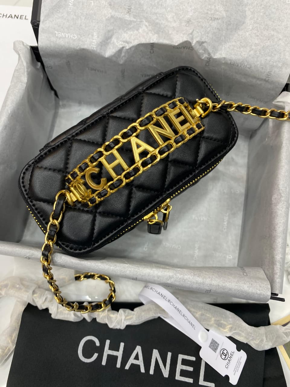 Black quilted handbag with gold chain and 'Cha nel' branding on a white background.
