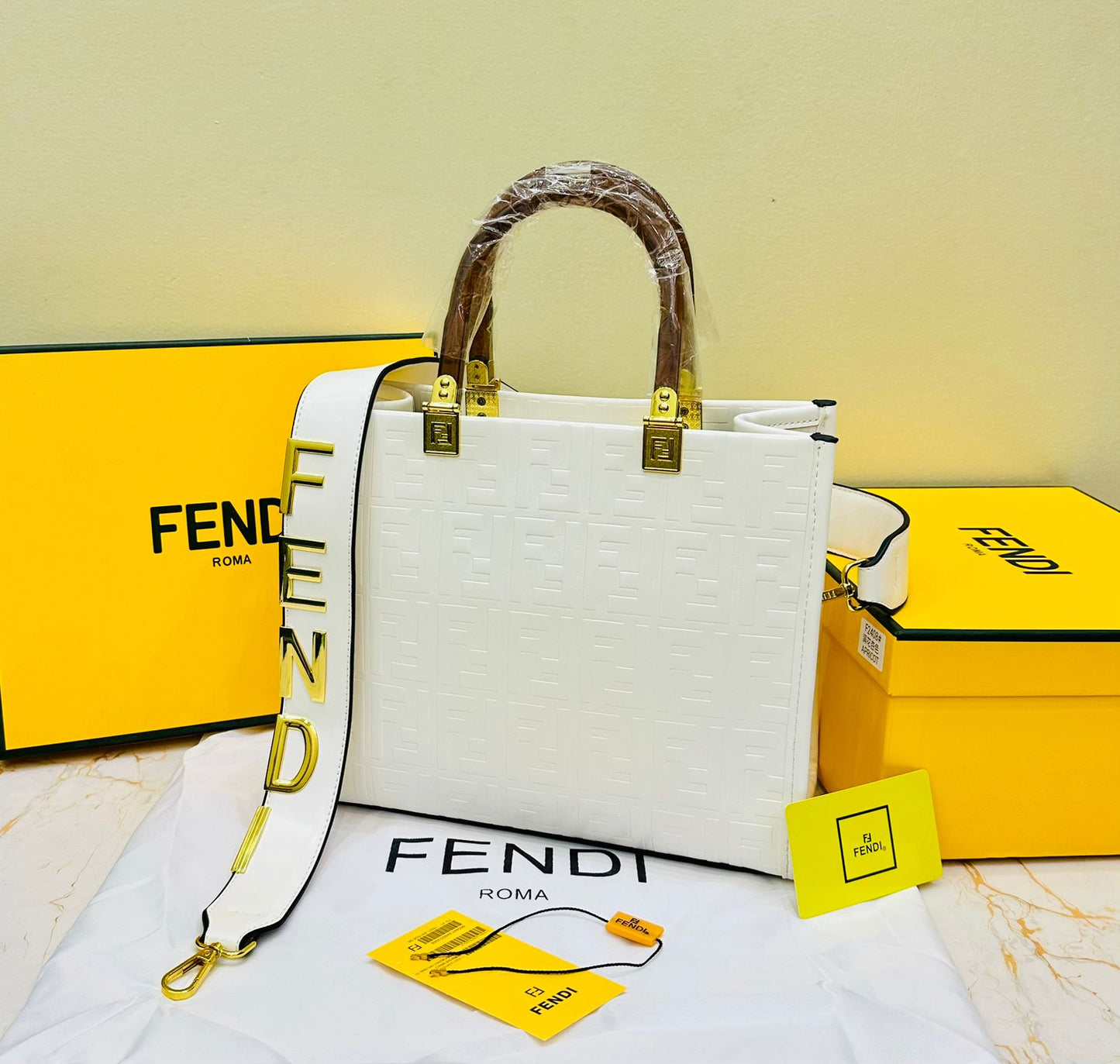 White Fen di handbag with yellow accents on a white surface with Fen di branded boxes in the background.