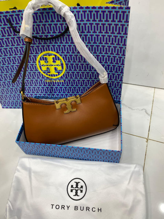 Brown handbag with gold clasp in a To ry Bur ch box on a white surface.