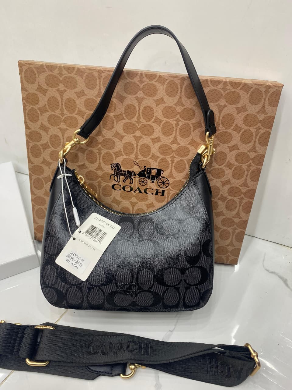 Co-ach handbag with a matching strap on a white surface with a brown box in the background.