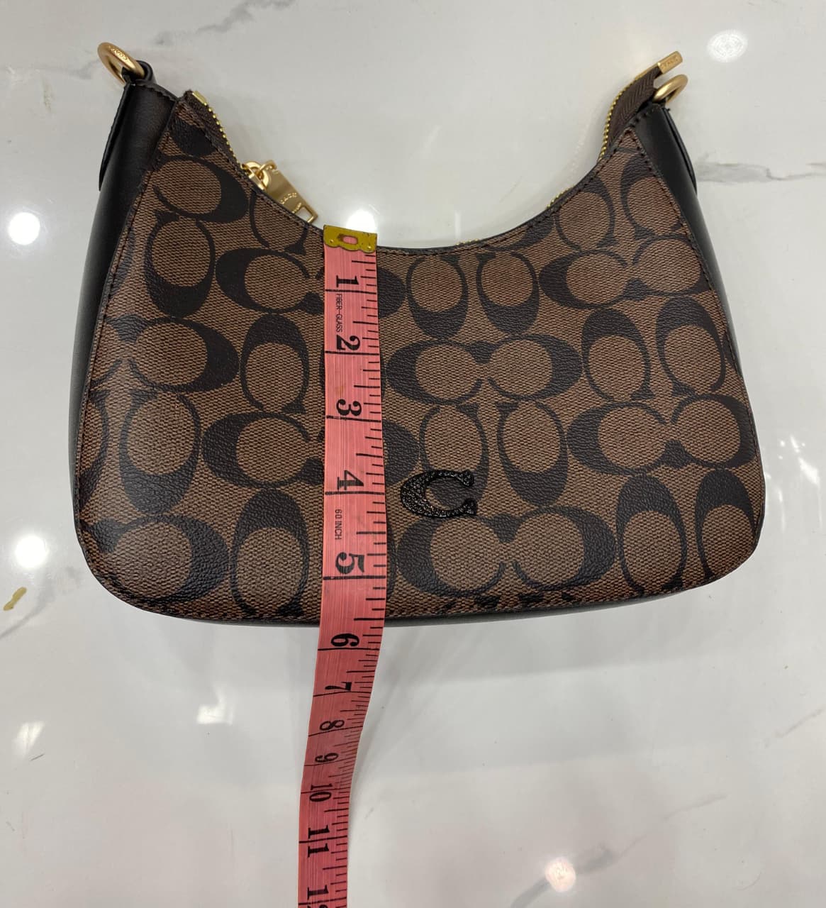 Co-ach handbag with a measuring tape for scale on a white background