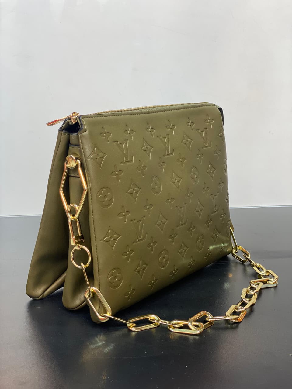 Green handbag with gold chain strap on a dark surface
