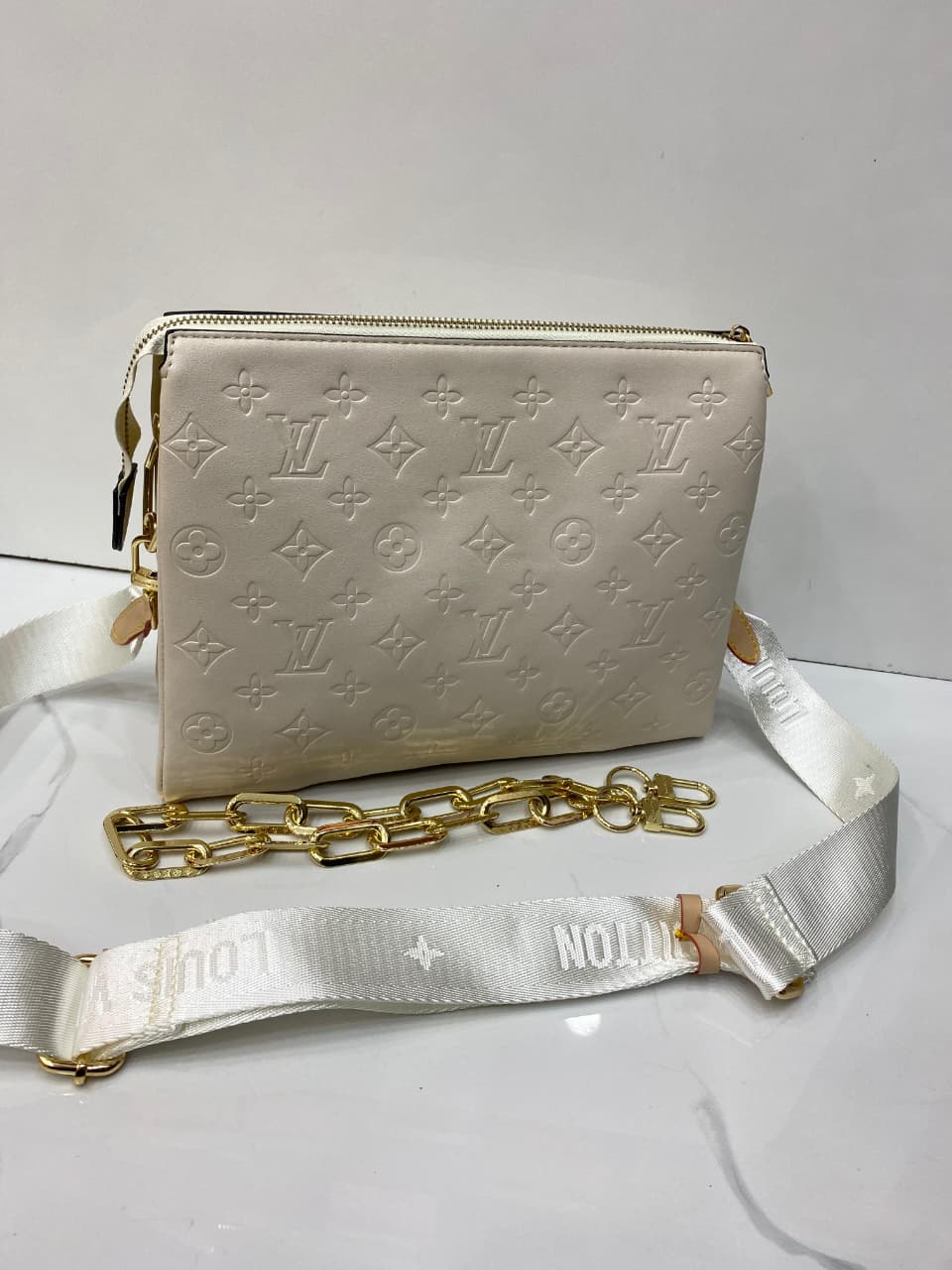White handbag with gold chain and white strap on a light gray background
