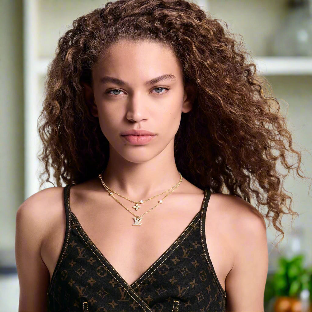 Woman wearing a black patterned top and gold necklace on a plain background
