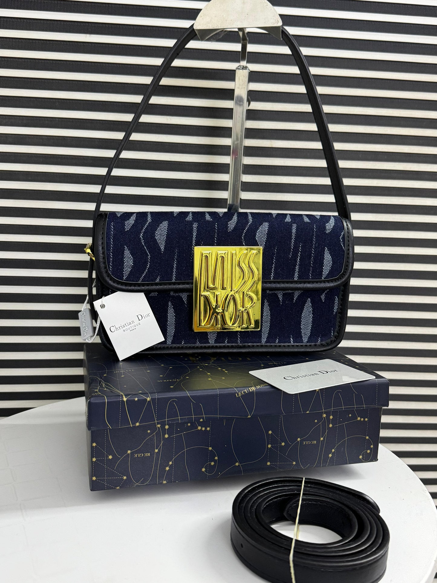 Navy handbag with gold logo on a matching box against a striped background