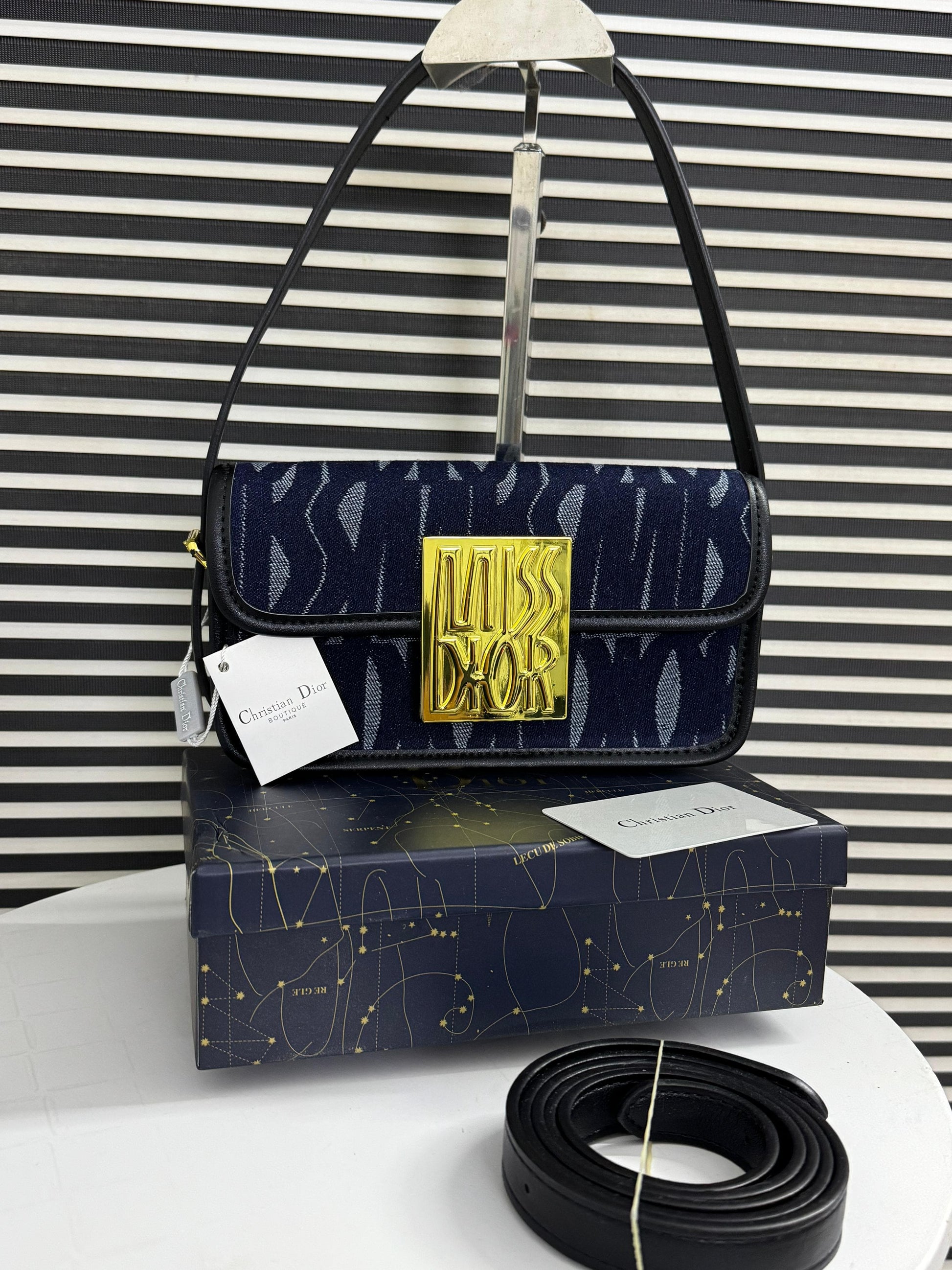 Navy handbag with gold logo on a matching box against a striped background
