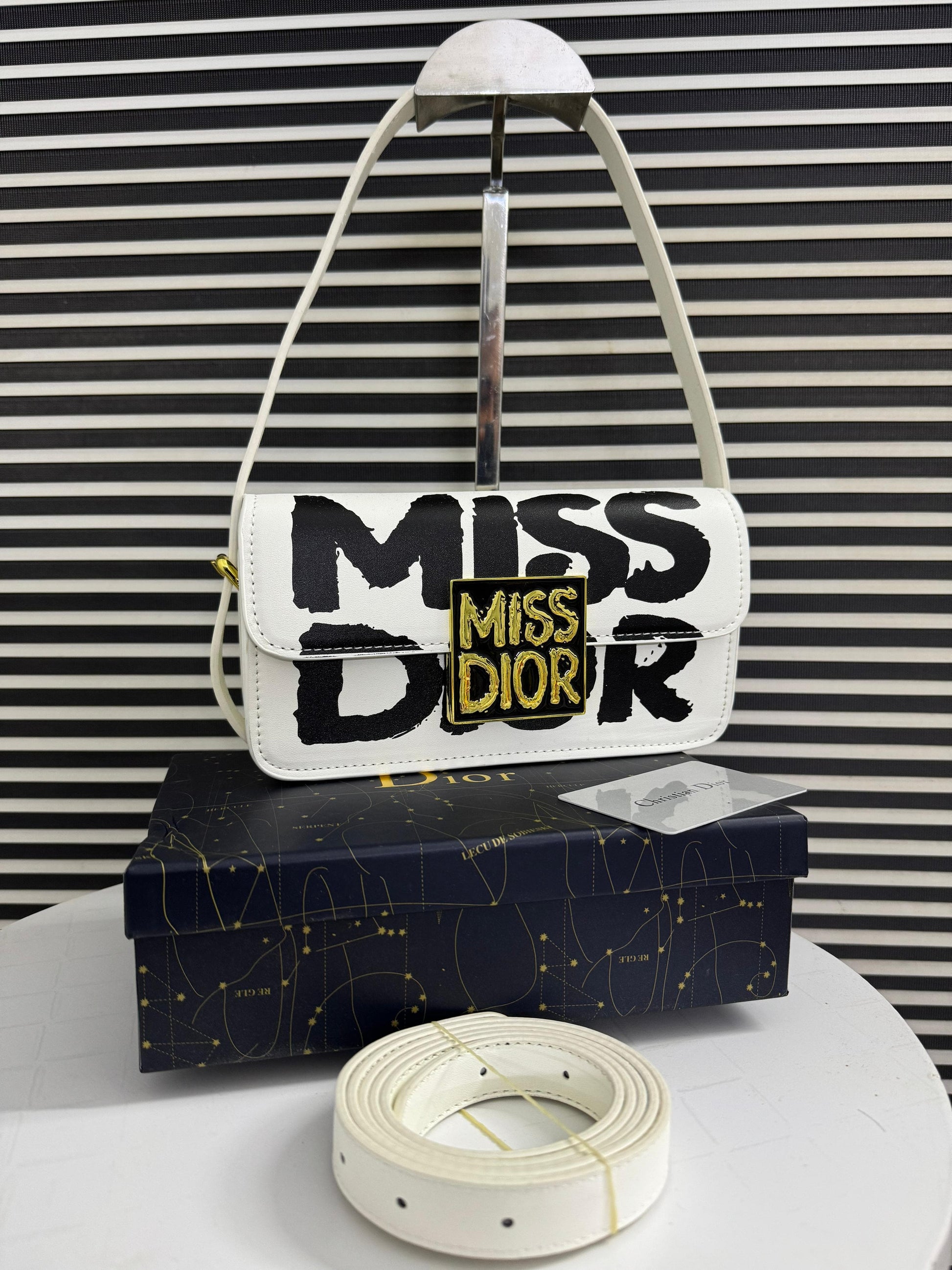 White handbag with 'MI SS DI OR' text on a black and white striped background