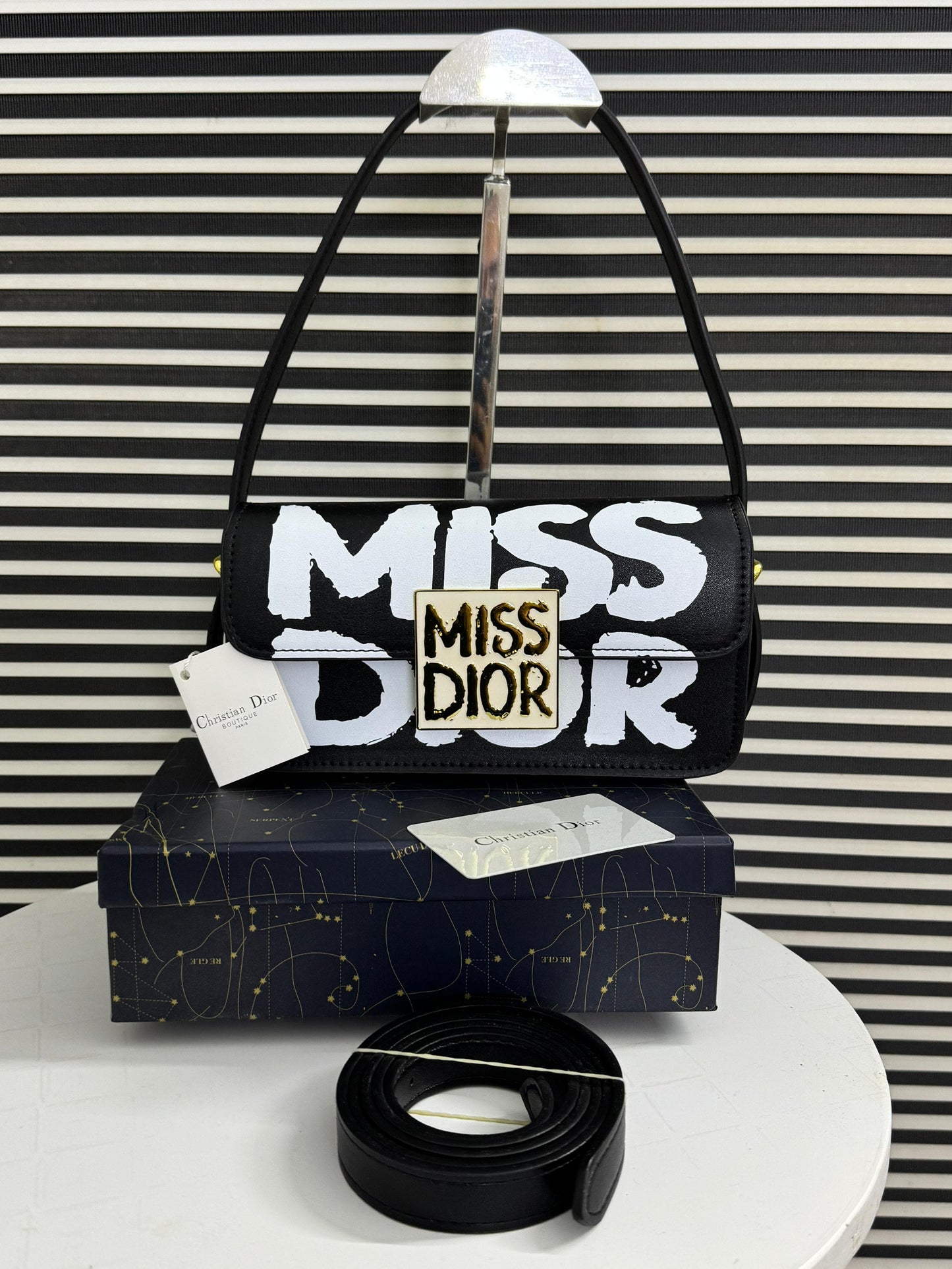 Black handbag with 'MI SS DI OR' text on a striped background