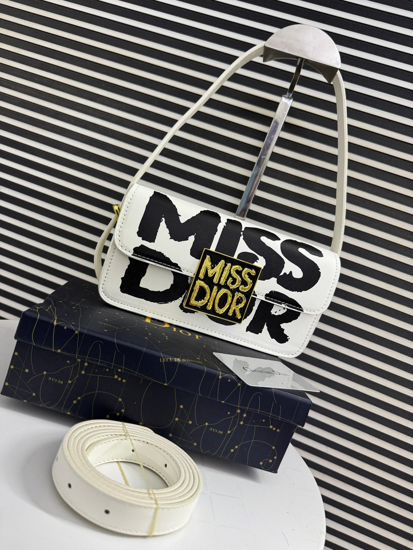 White handbag with 'Mi ss Di or' text on a striped background