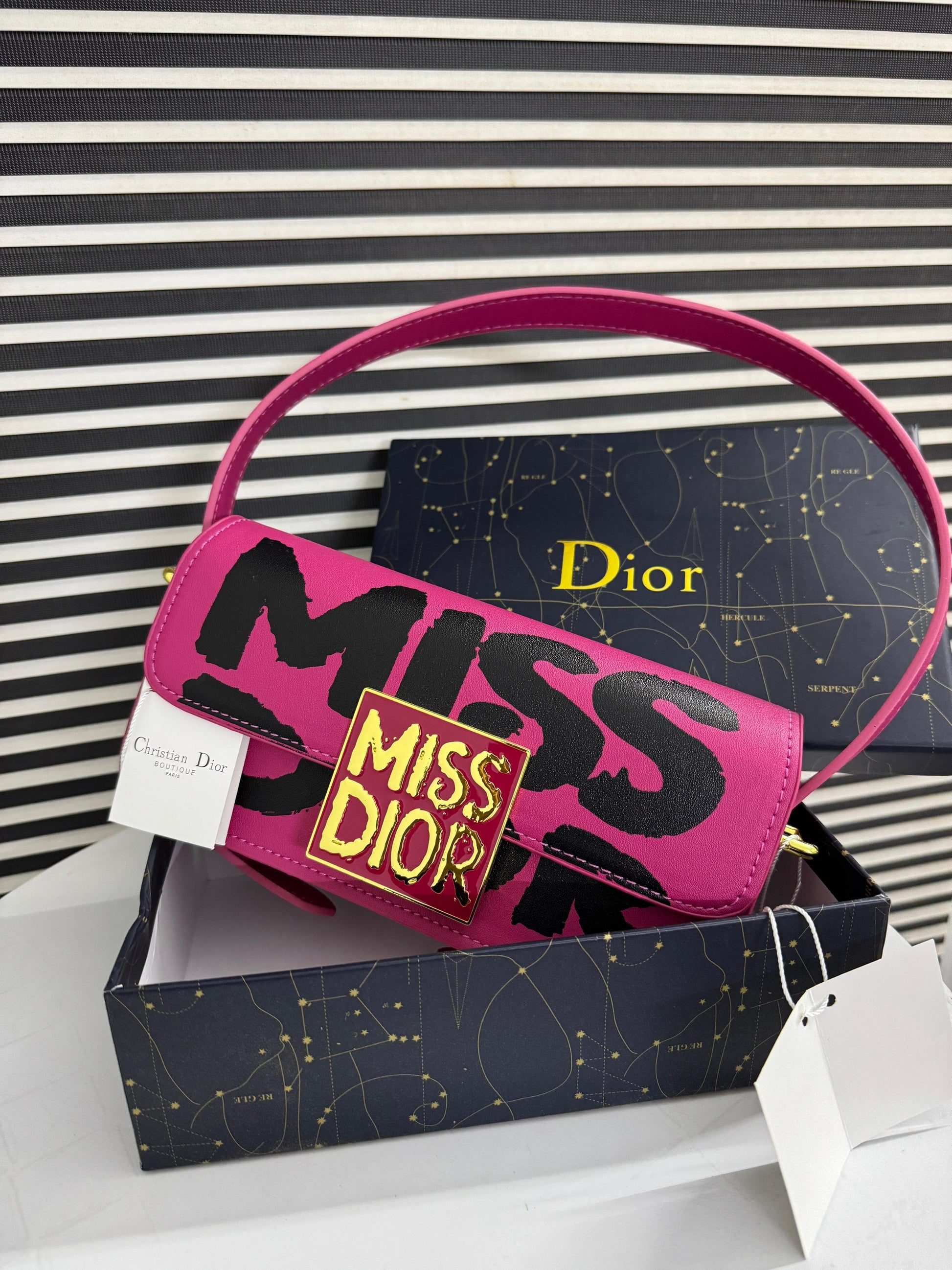 Pink Di or handbag with 'Mi ss Di or' text on a black and white striped background