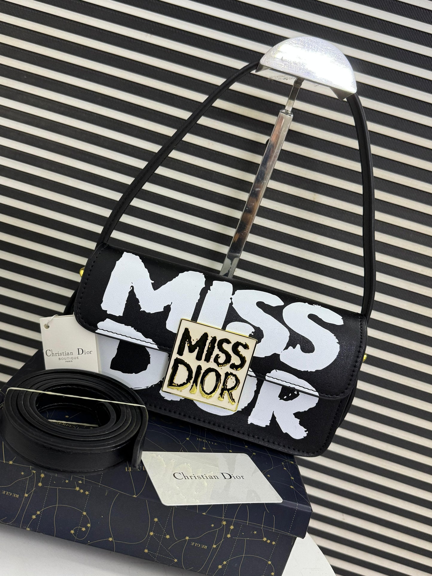 Black handbag with 'Mi ss Di or' text on a striped background