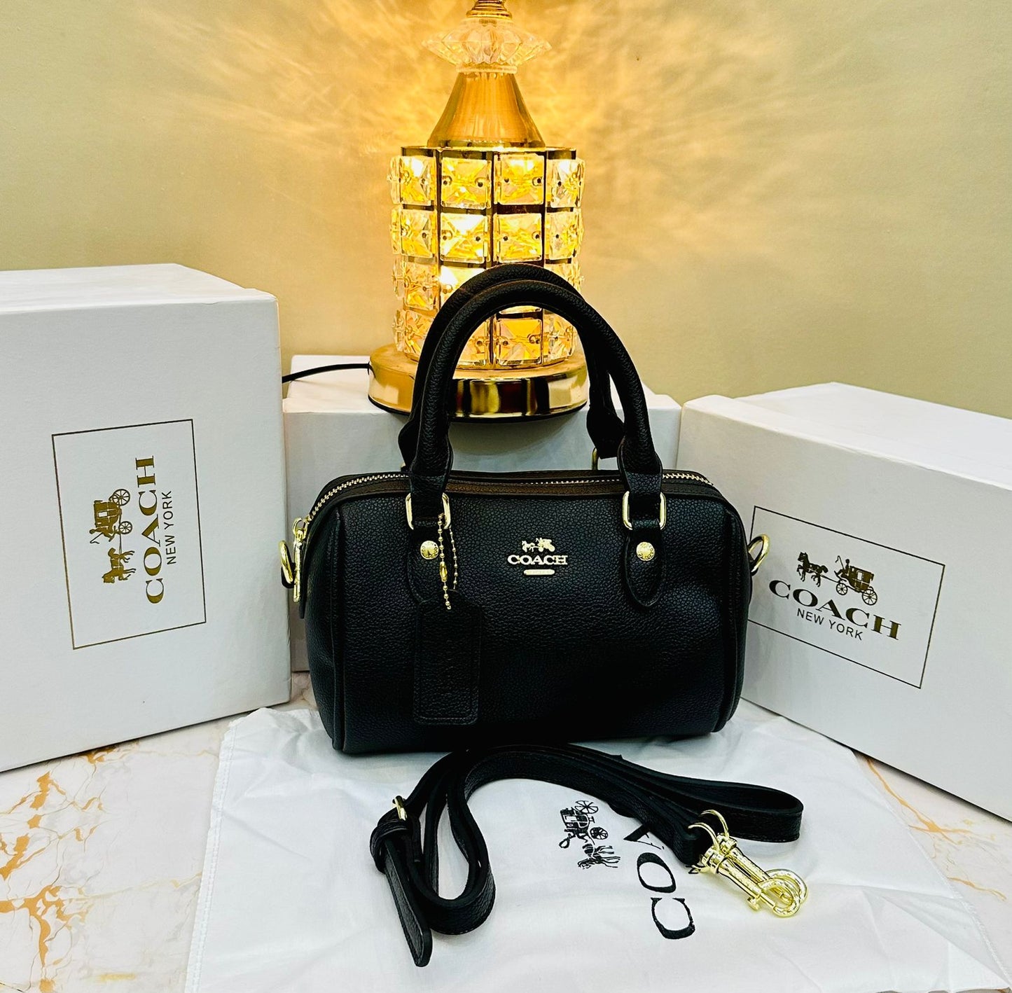 Black Co ach handbag with gold accents on a white surface with Co ach branding in the background.