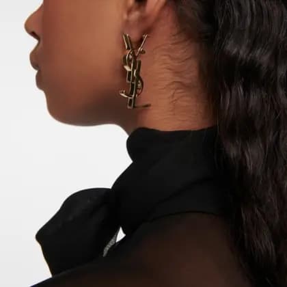 Close-up of a person wearing a gold earring with a logo on a plain background