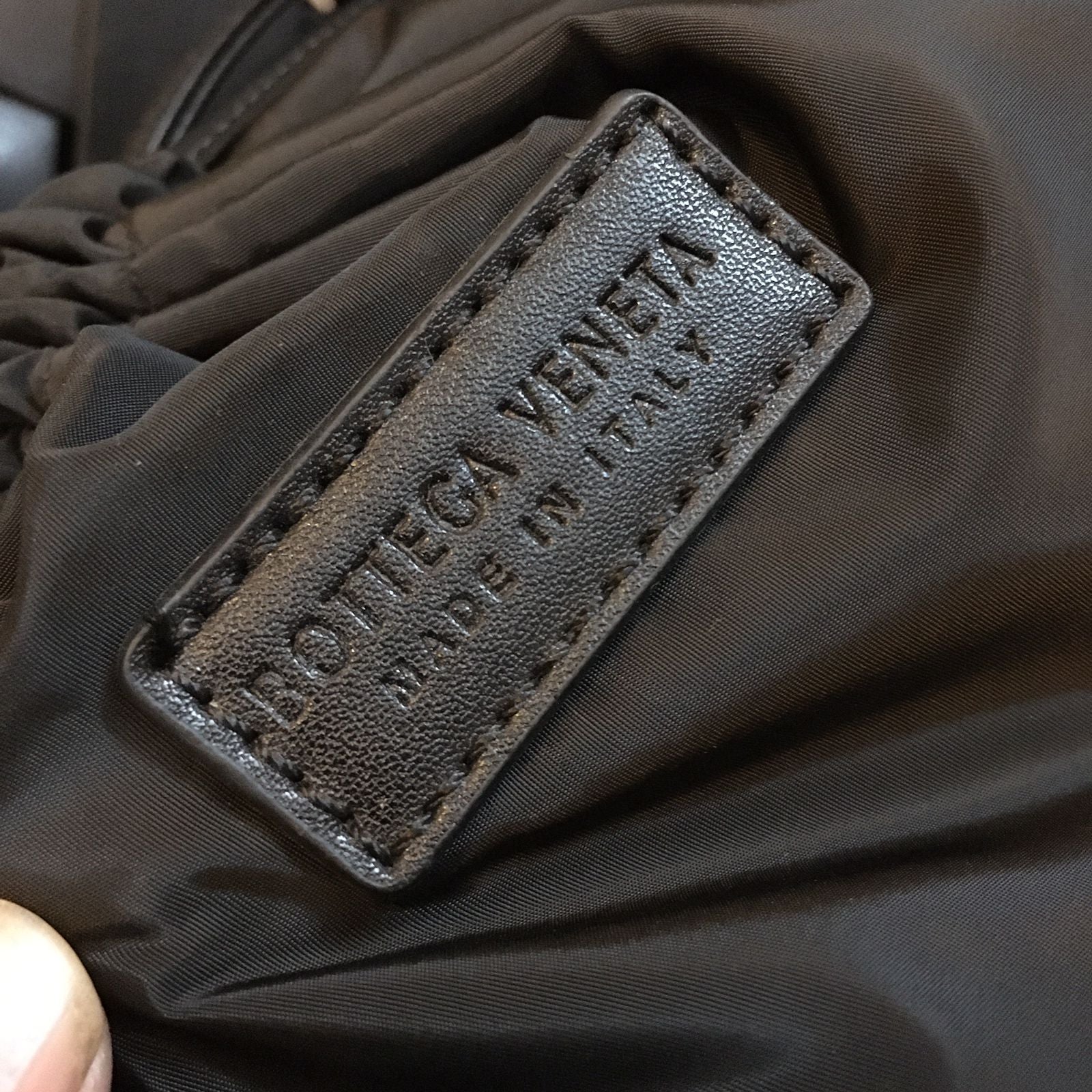 Close-up of a label on a dark fabric, likely a garment, with 'Bott-ega Ven-eta' branding.