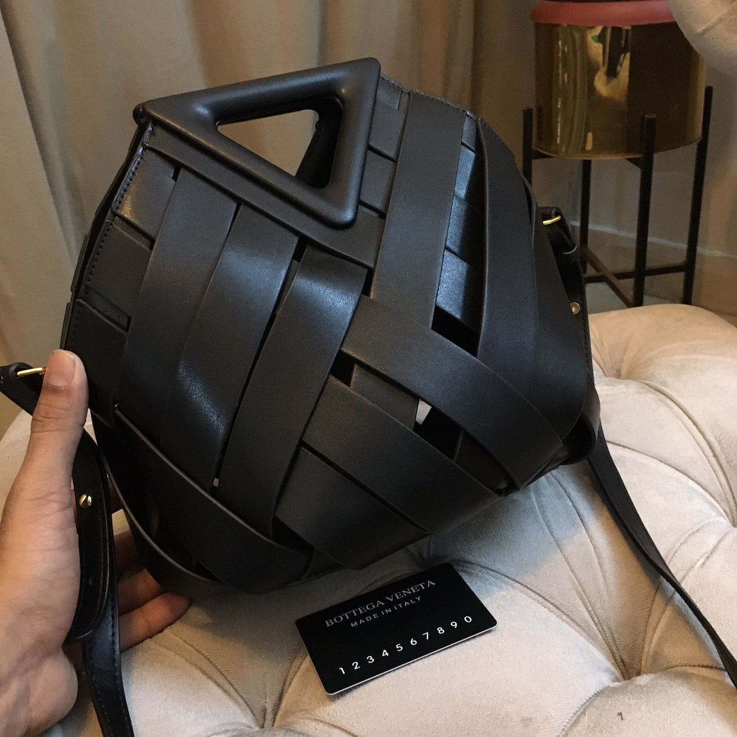 Black woven handbag held by a person on a beige surface with a blurred background