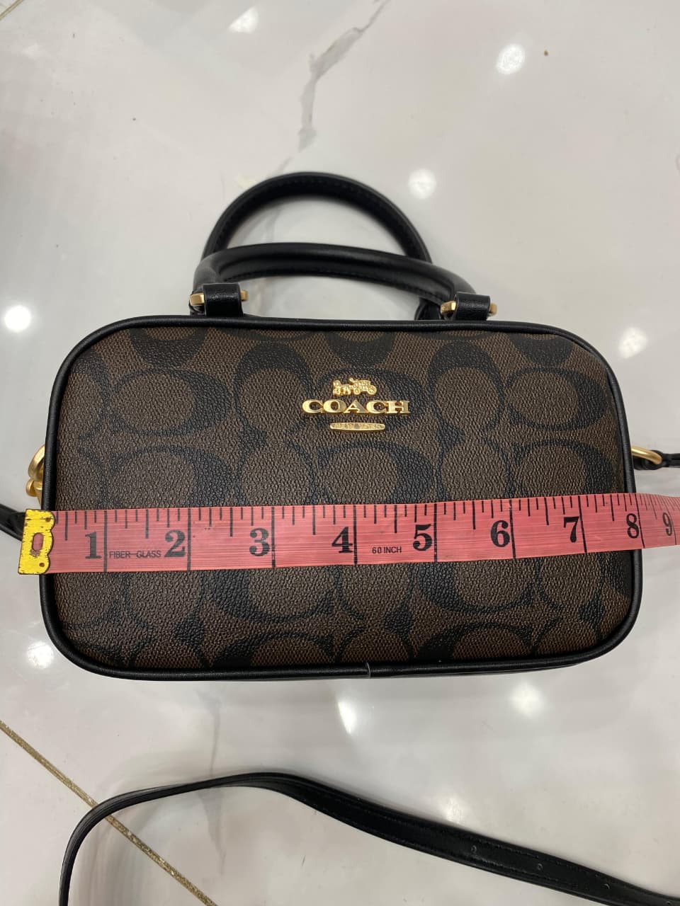 Co-ach handbag with a measuring tape on a white surface