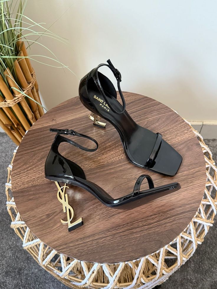 Black high-heeled shoes on a wooden table with a plant in the background