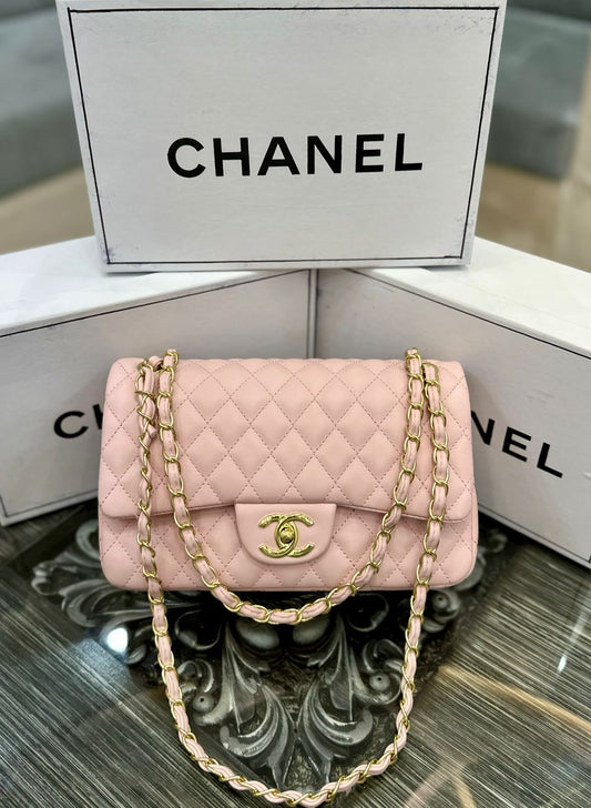 Pink Cha nel handbag with gold chain and logo on a reflective surface with Cha nel branding in the background.