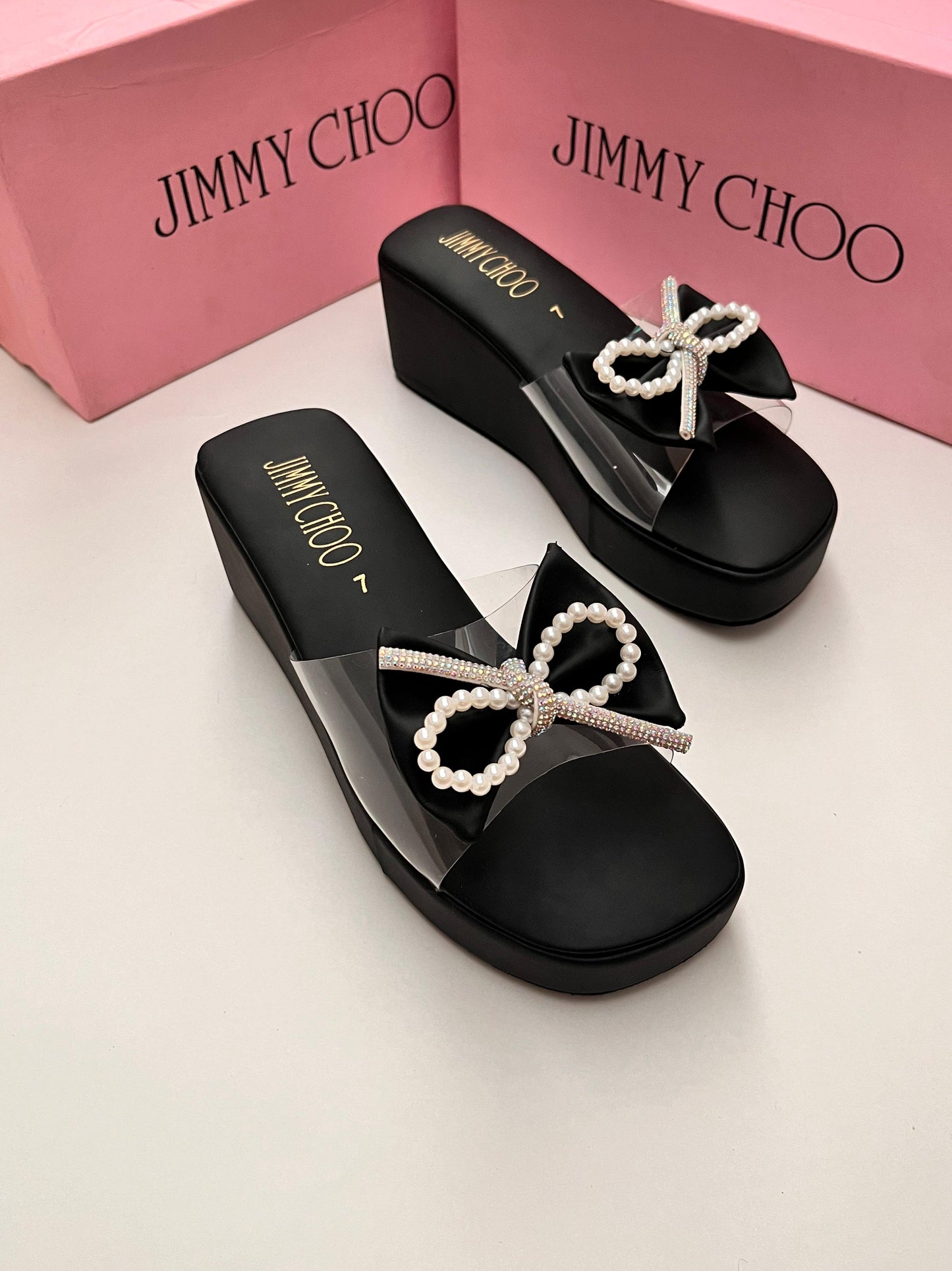 Black sandals with pearl bows on a light background, featuring Jim my Ch oo branding.