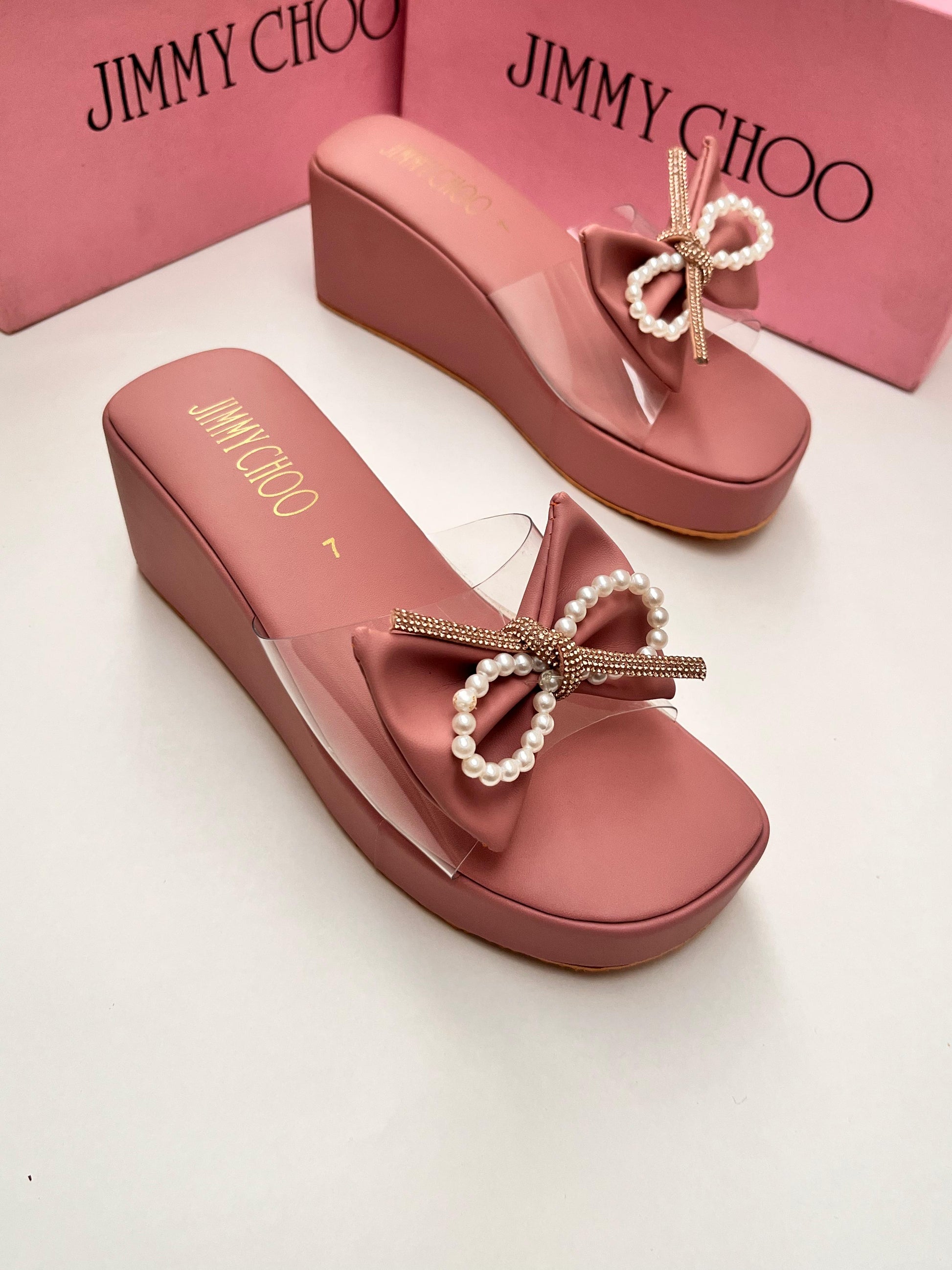 Pink wedge sandals with decorative bows on a white background, featuring Jim my Ch oo branding.