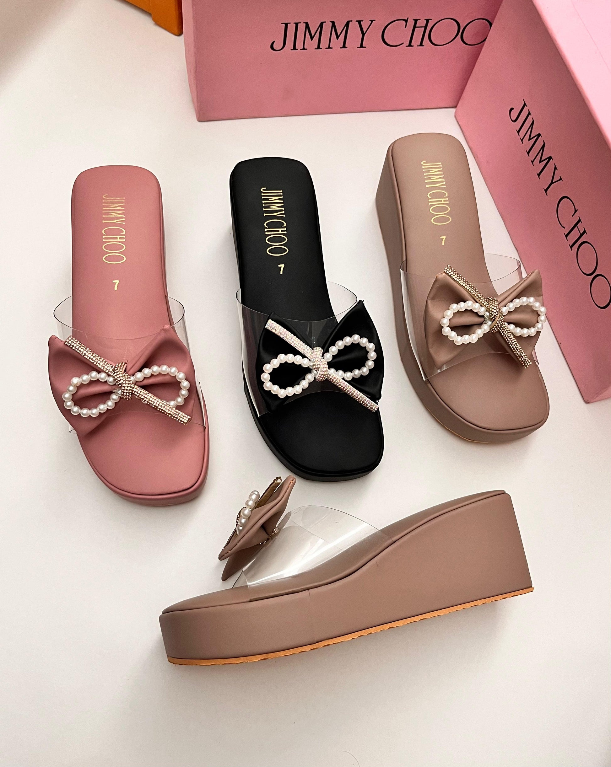 Three pairs of Jim my Ch oo sandals in pink, black, and brown with pearl bows on a white background.