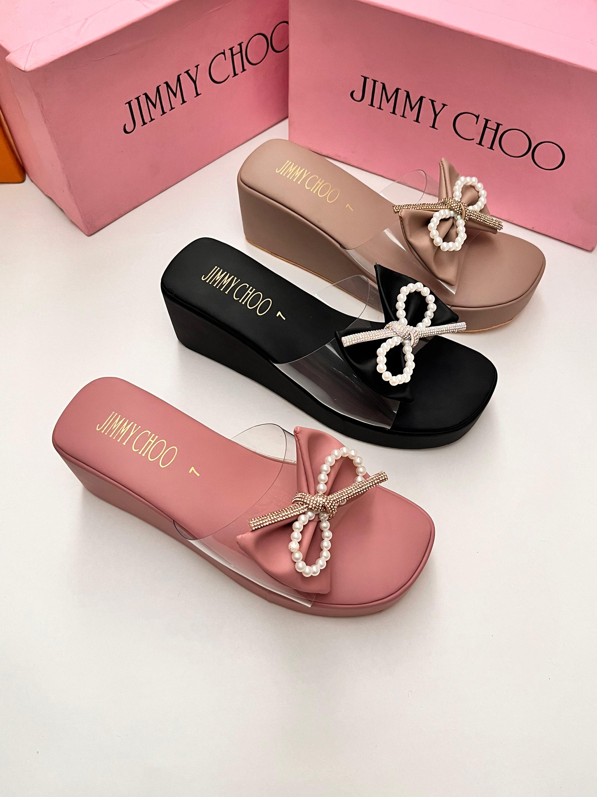 Jimmy Choo sandals in black, pink, and beige with pearl embellishments on a white background.