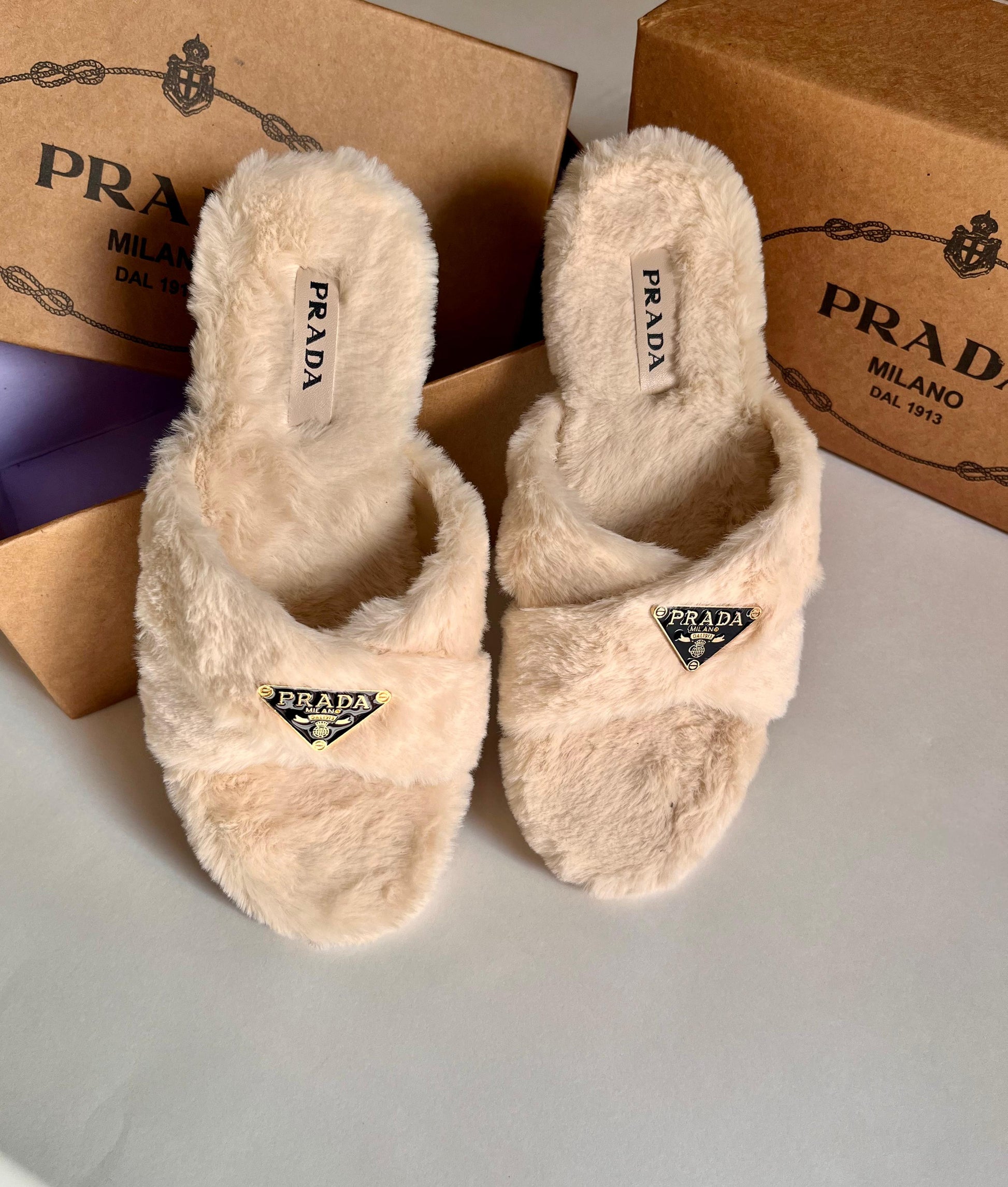 Pair of fluffy Pra da slippers with branded boxes in the background.