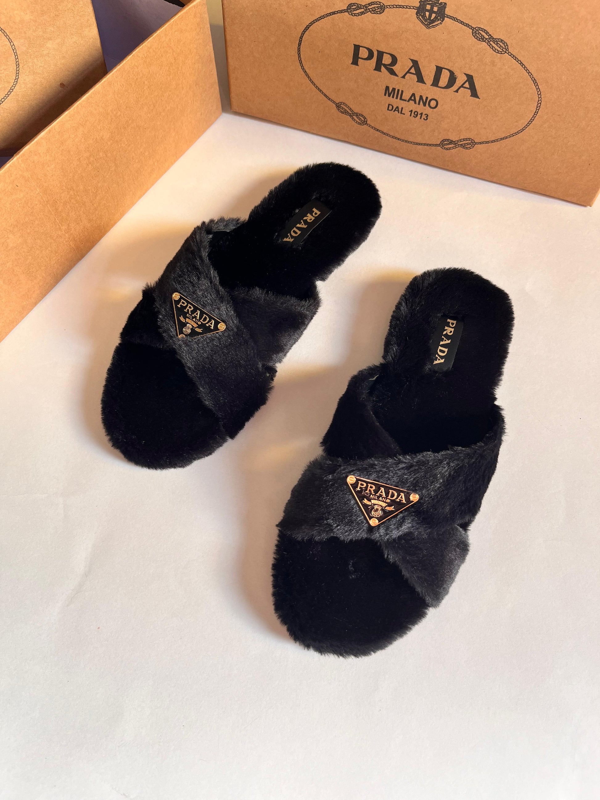 Black Pra da slippers with fur on a white surface, featuring a Pra da box in the background.