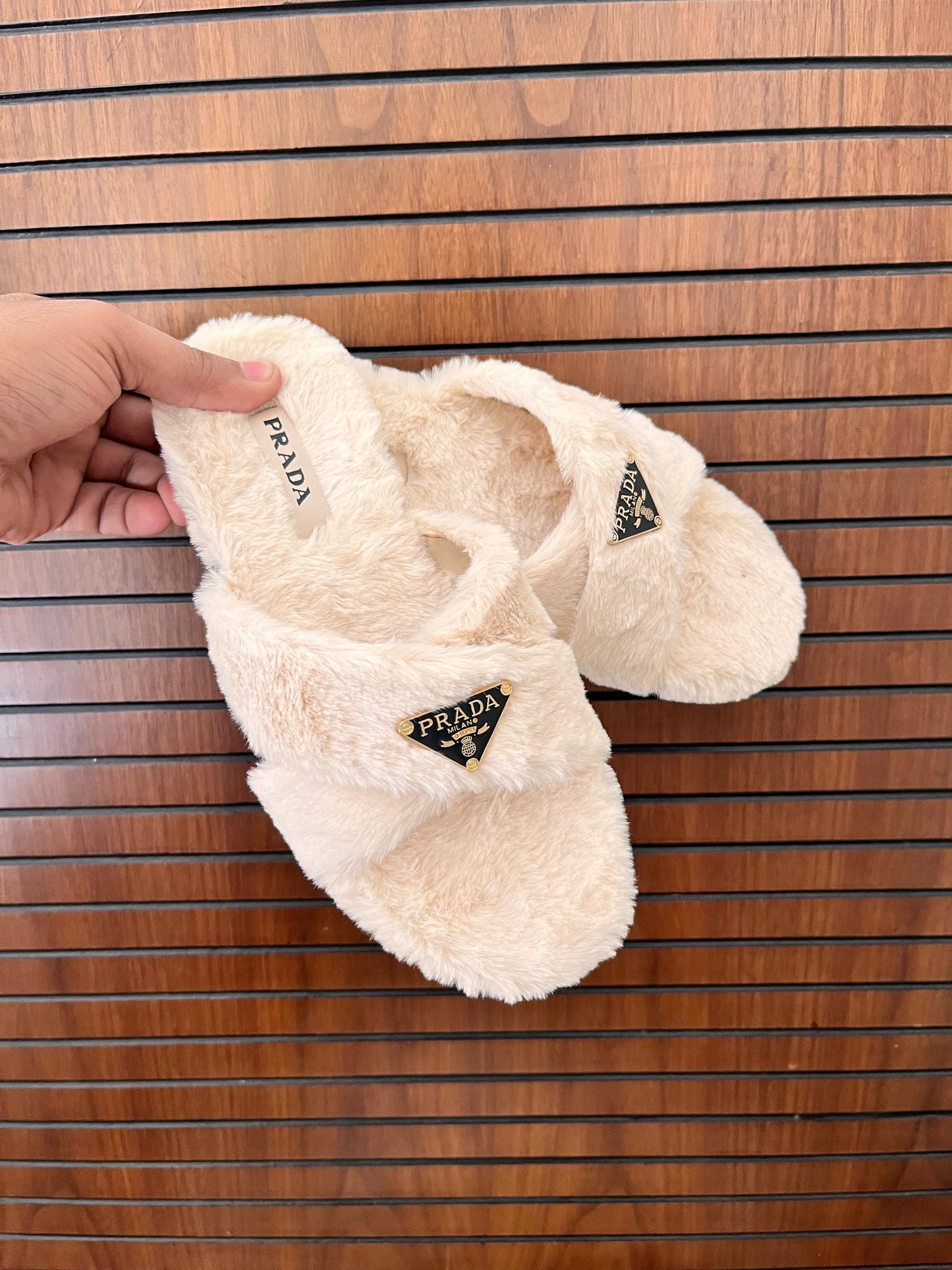 Beige fuzzy slippers with Pra da logo on a wooden surface
