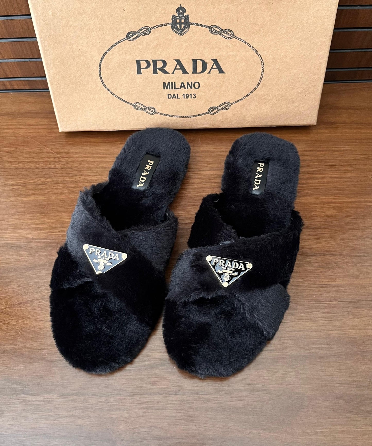 Black Pra da slippers on a wooden surface with a Pra da box in the background.