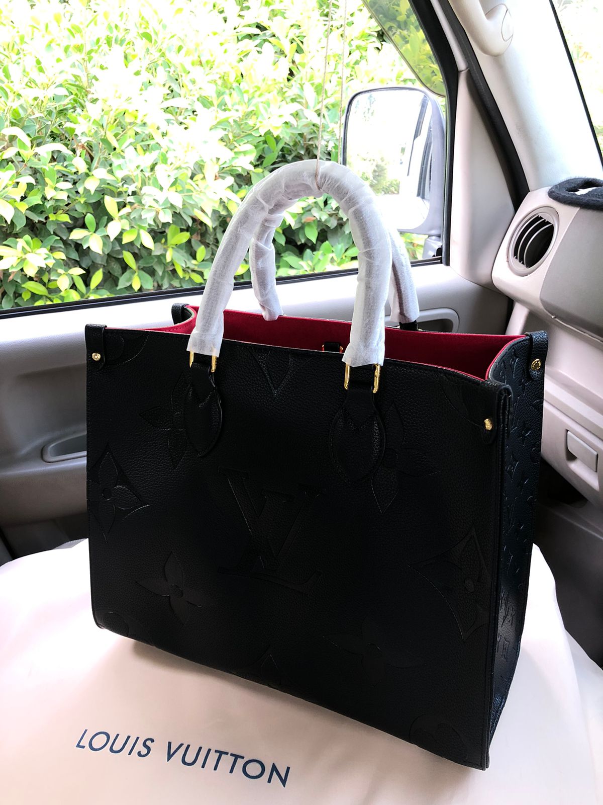 Black Lou is Vui tton handbag with white handles inside a car.