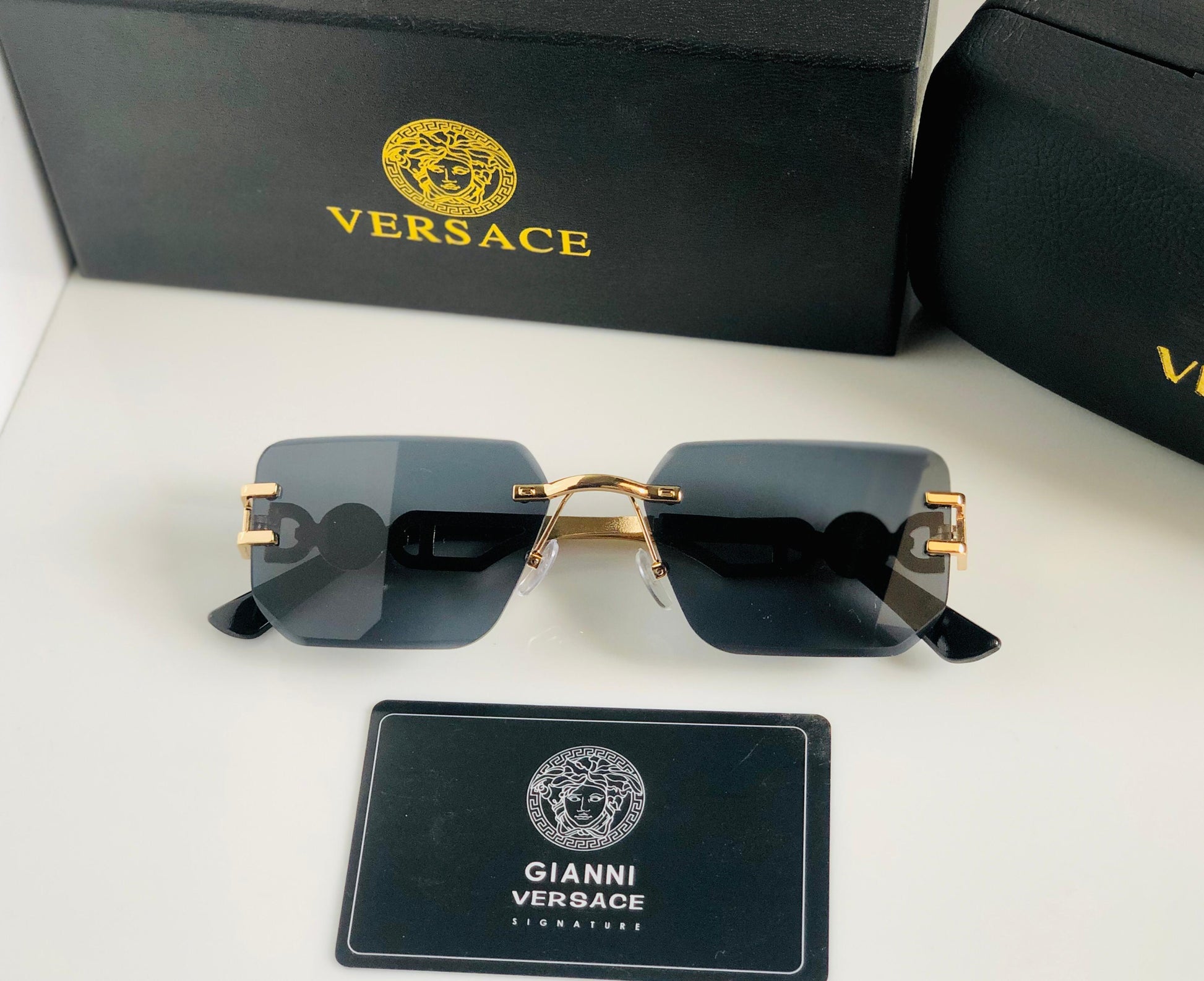 Ver sace sunglasses with gold frames and black lenses, displayed with Versace packaging on a white background.